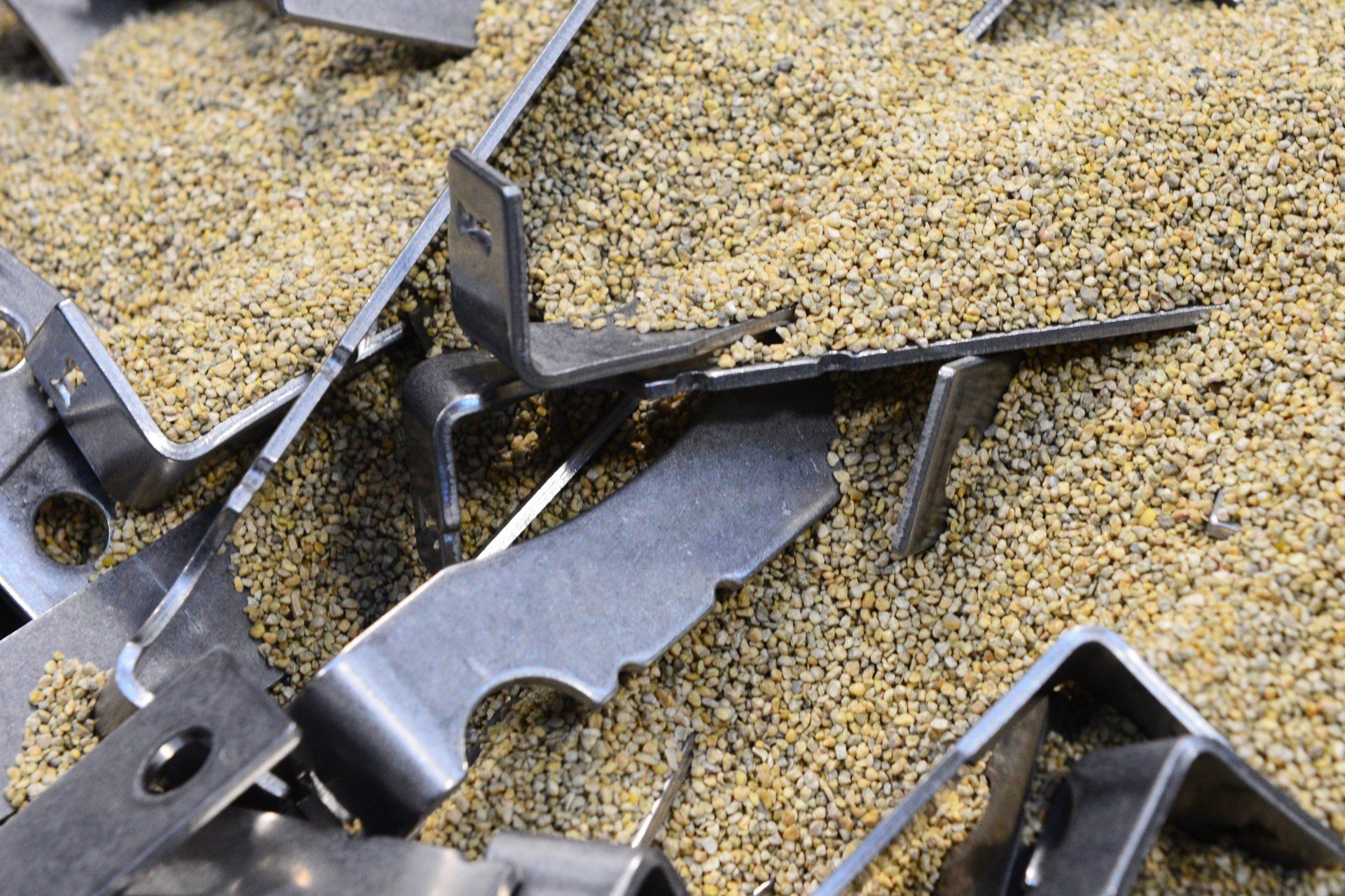 Parti di staffe metalliche in un letto di piccoli granuli color beige.