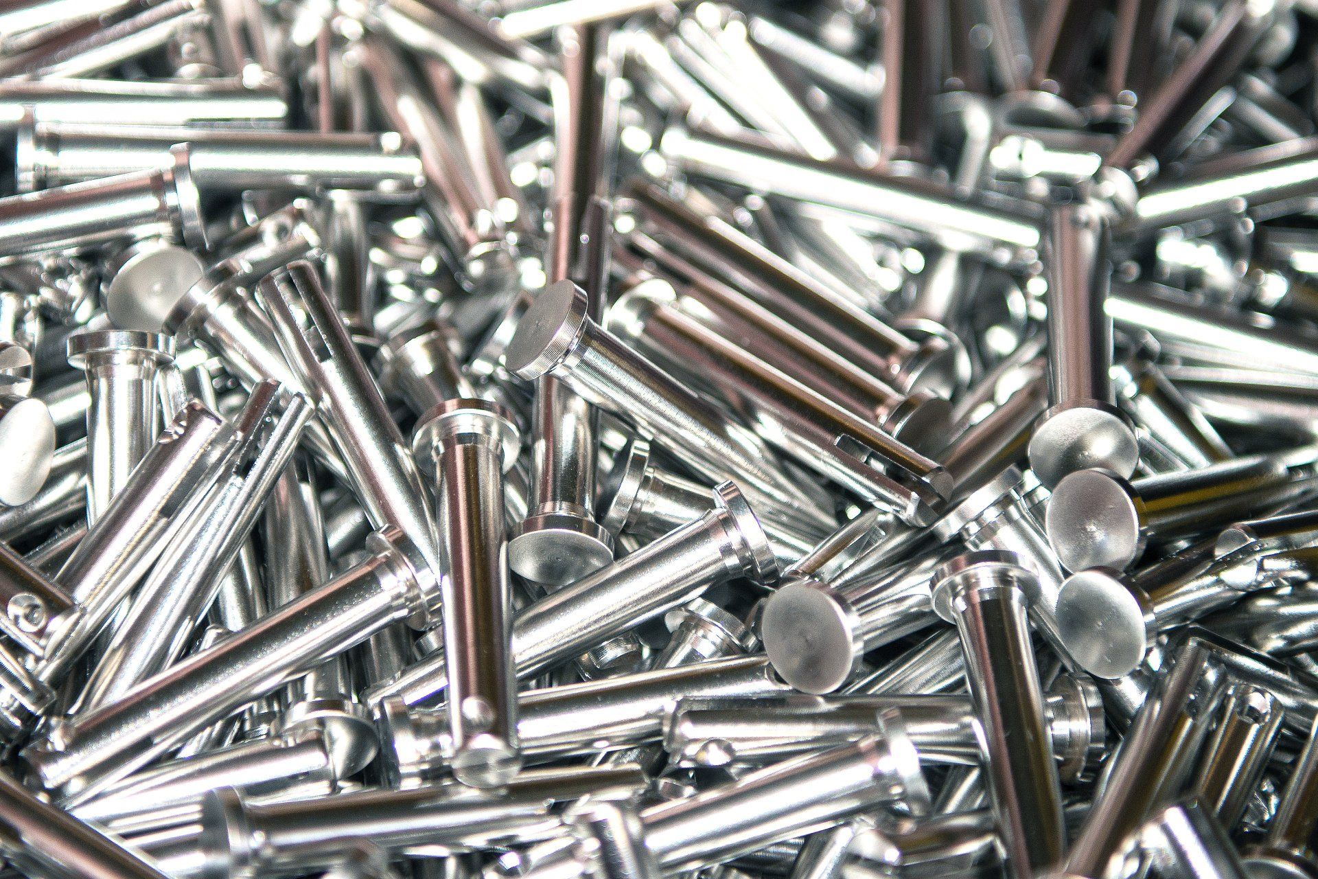 Mucchio di rivetti metallici lucidi, con teste circolari piatte, accatastati uno vicino all'altro.