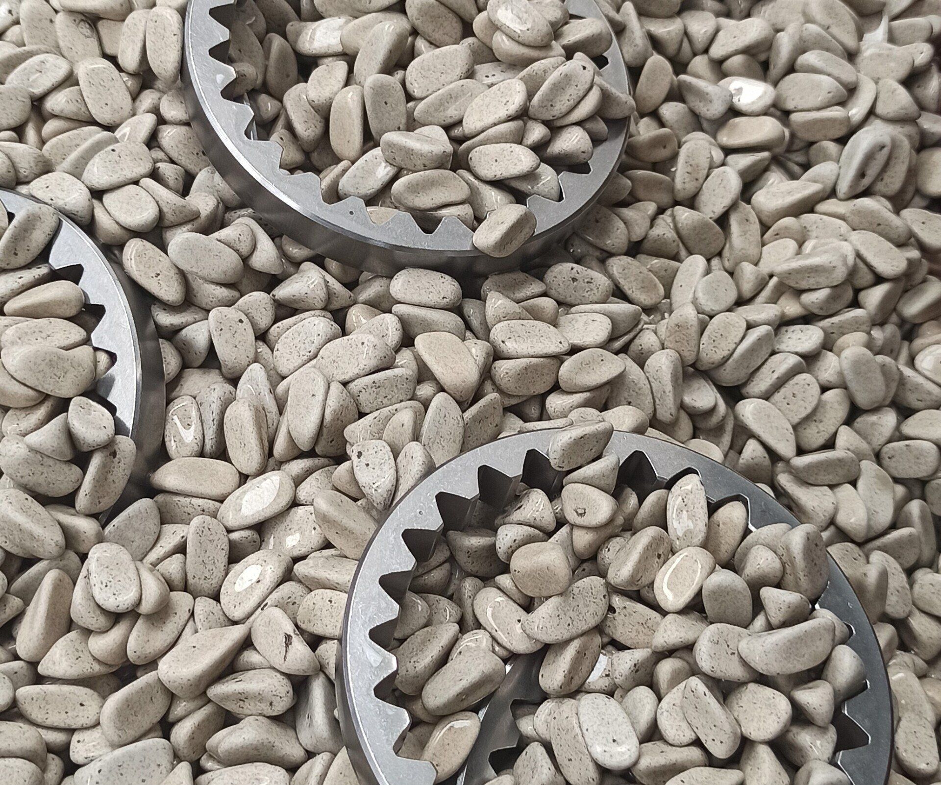 Primo piano di numerose pietre grigie di forma ovale mescolate a oggetti metallici simili a ingranaggi.