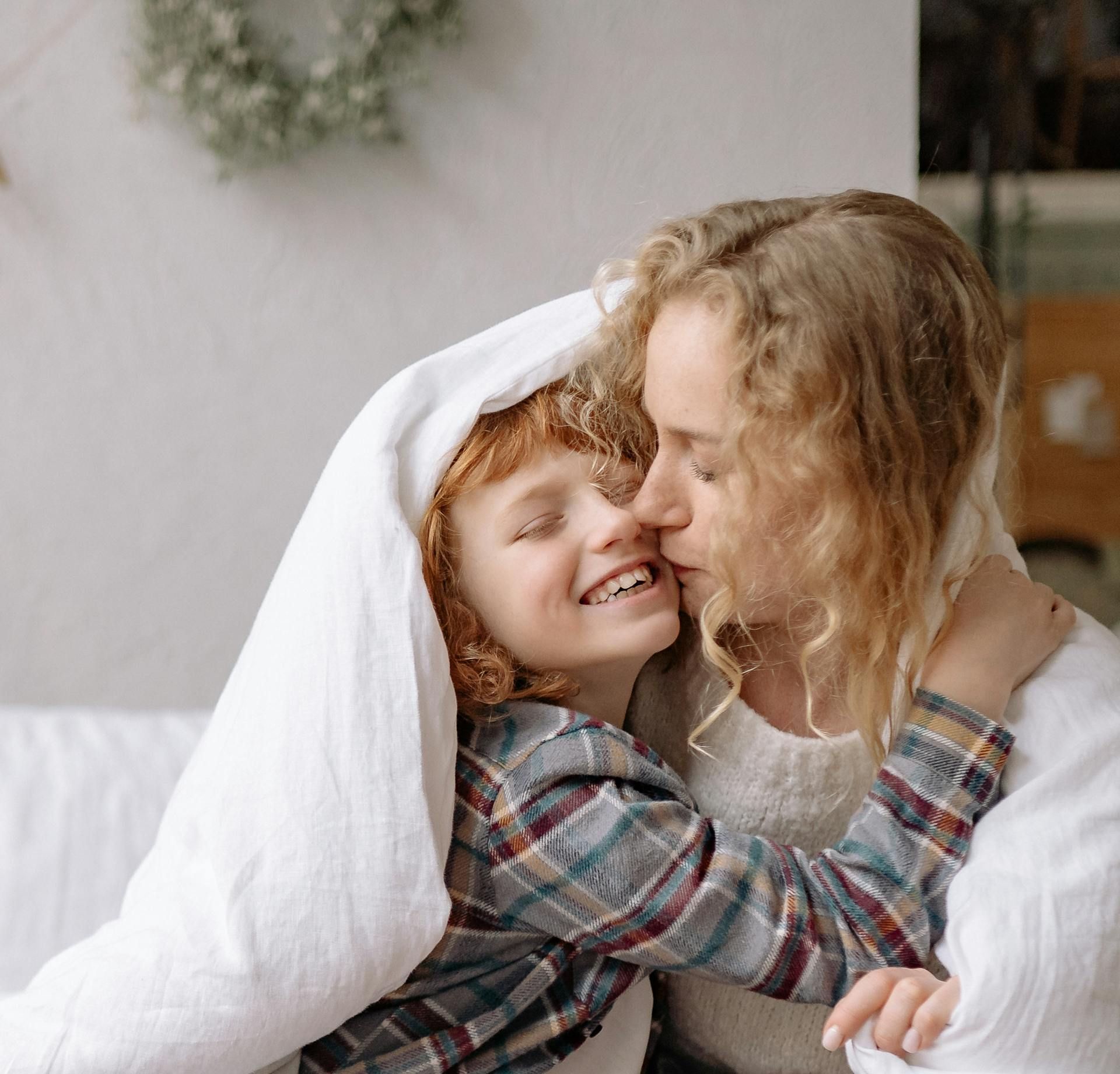 A woman and a child are hugging under a blanket.