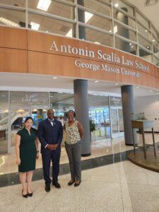 Three people pose in front of the Antonin Scalia Law School entrance at George Mason University.