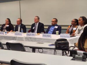 Panel of six people seated at a table, participating in a discussion.