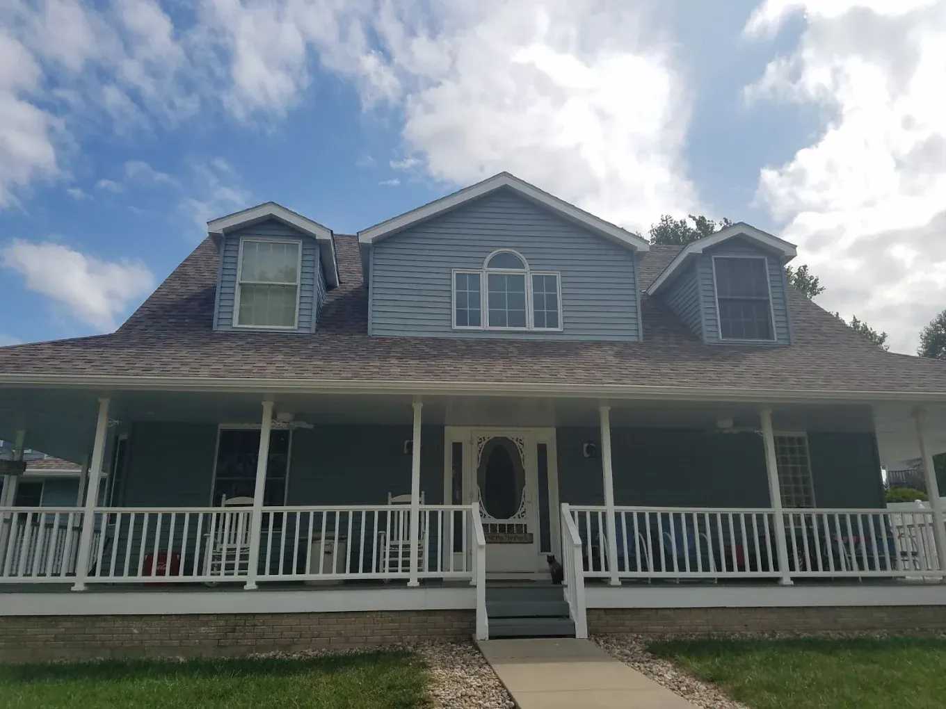 Blue two-story house with a wraparound porch, white trim, and a cloudy sky.