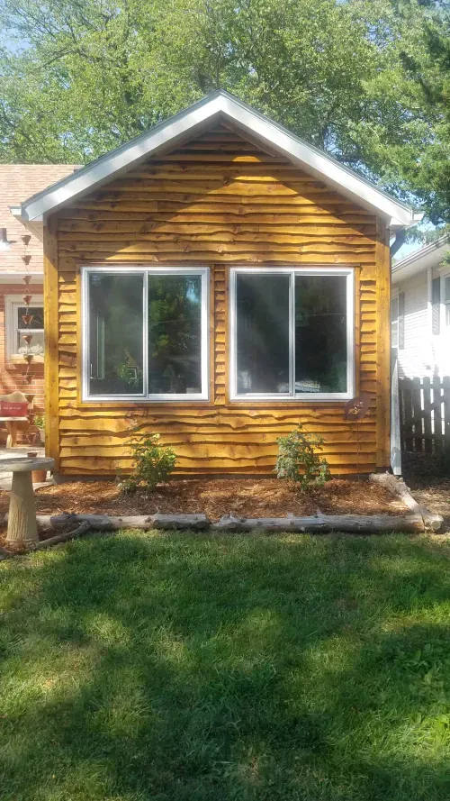 Small, wooden building with two windows, brown siding, and a grassy yard.