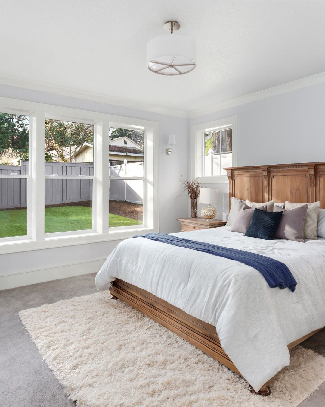 Bedroom with a wooden bed, large windows, white bedding, and a fluffy rug.
