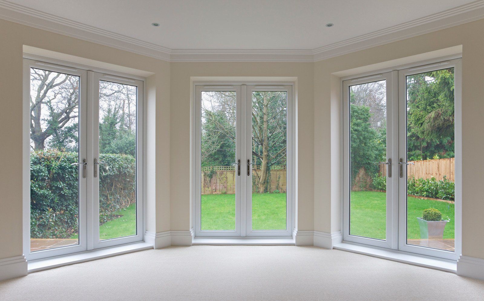 Light-filled room with three sets of double-pane glass doors overlooking a green lawn and trees.