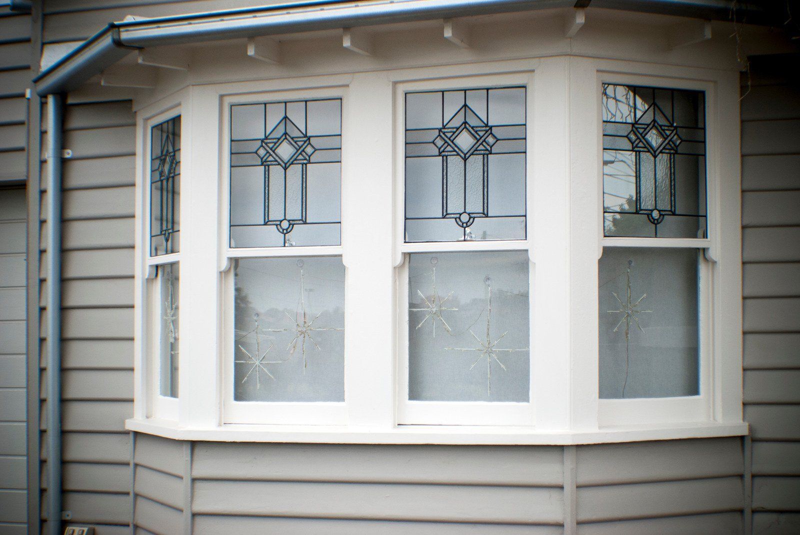Bay window with white frame and stained glass, on a grey house.