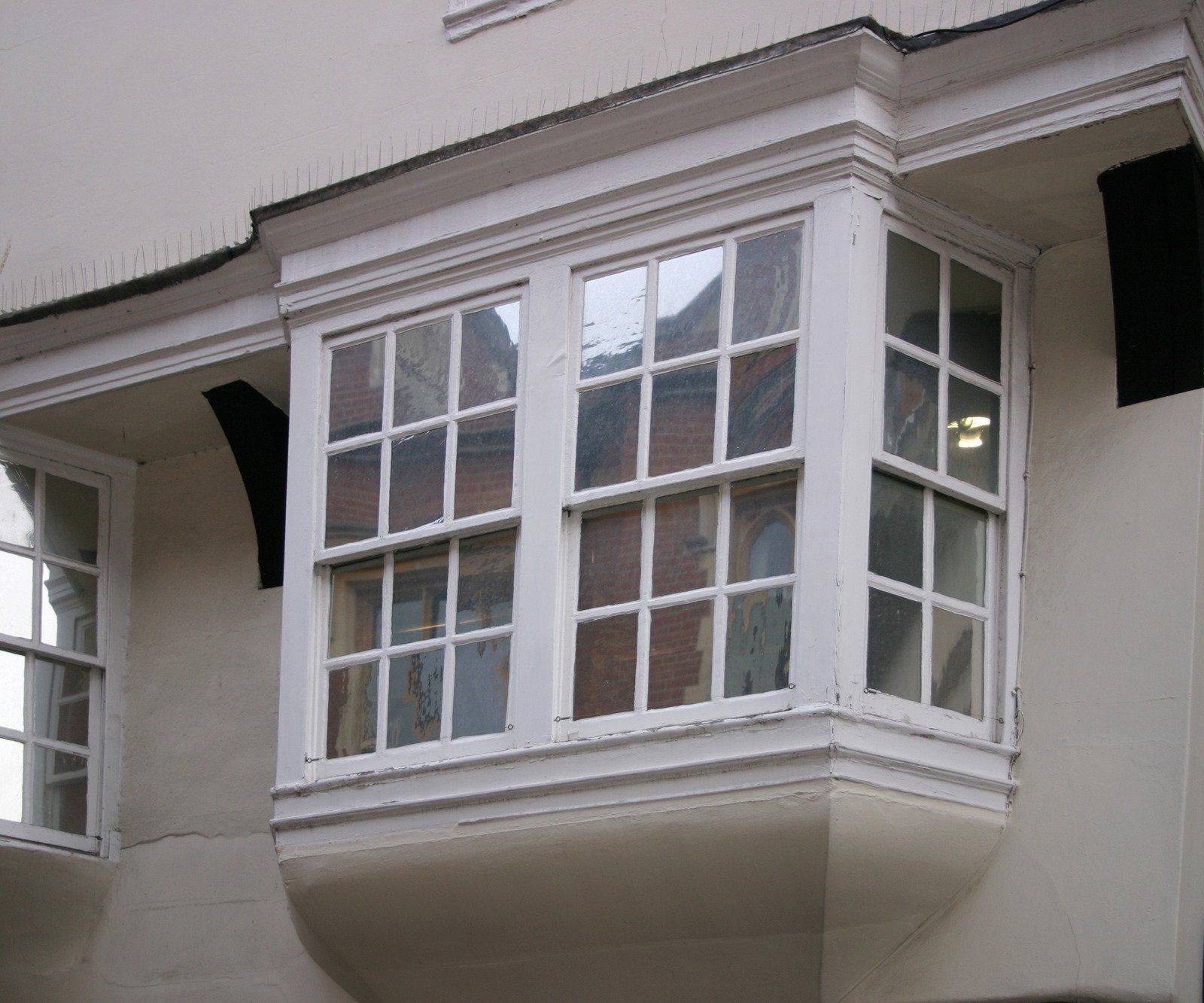 White bay window on a cream-colored building, angled glass panels with divided panes.