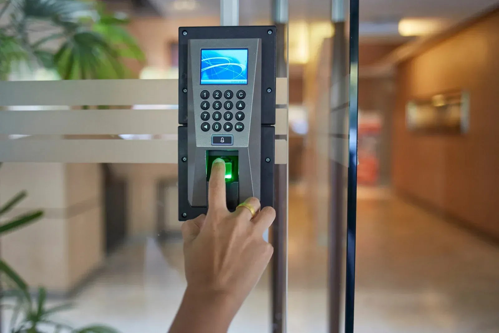 Person using fingerprint scanner on a glass door. The scanner is mounted on a metal plate.