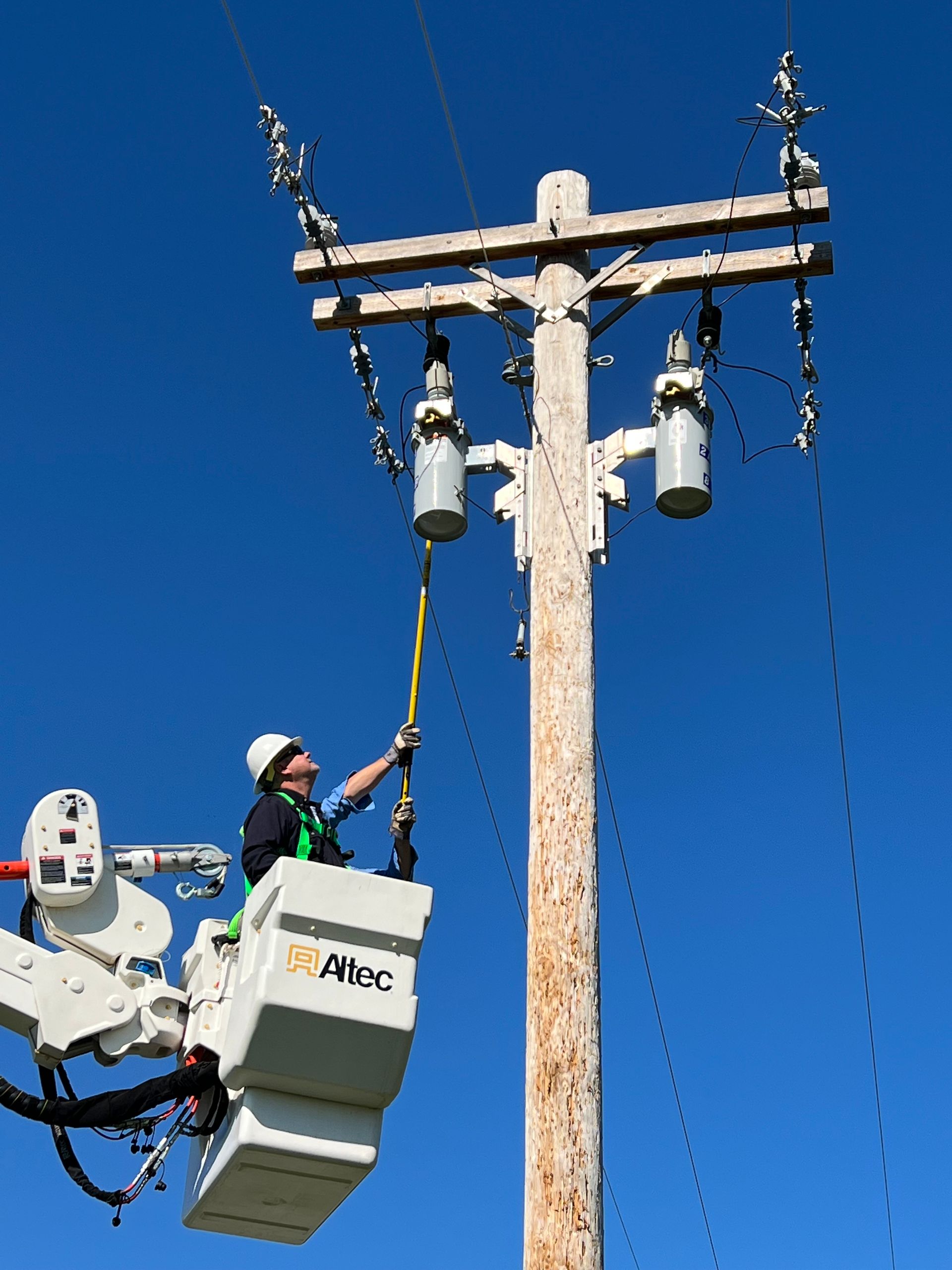 A man is sitting in a bucket on top of an electrical pole