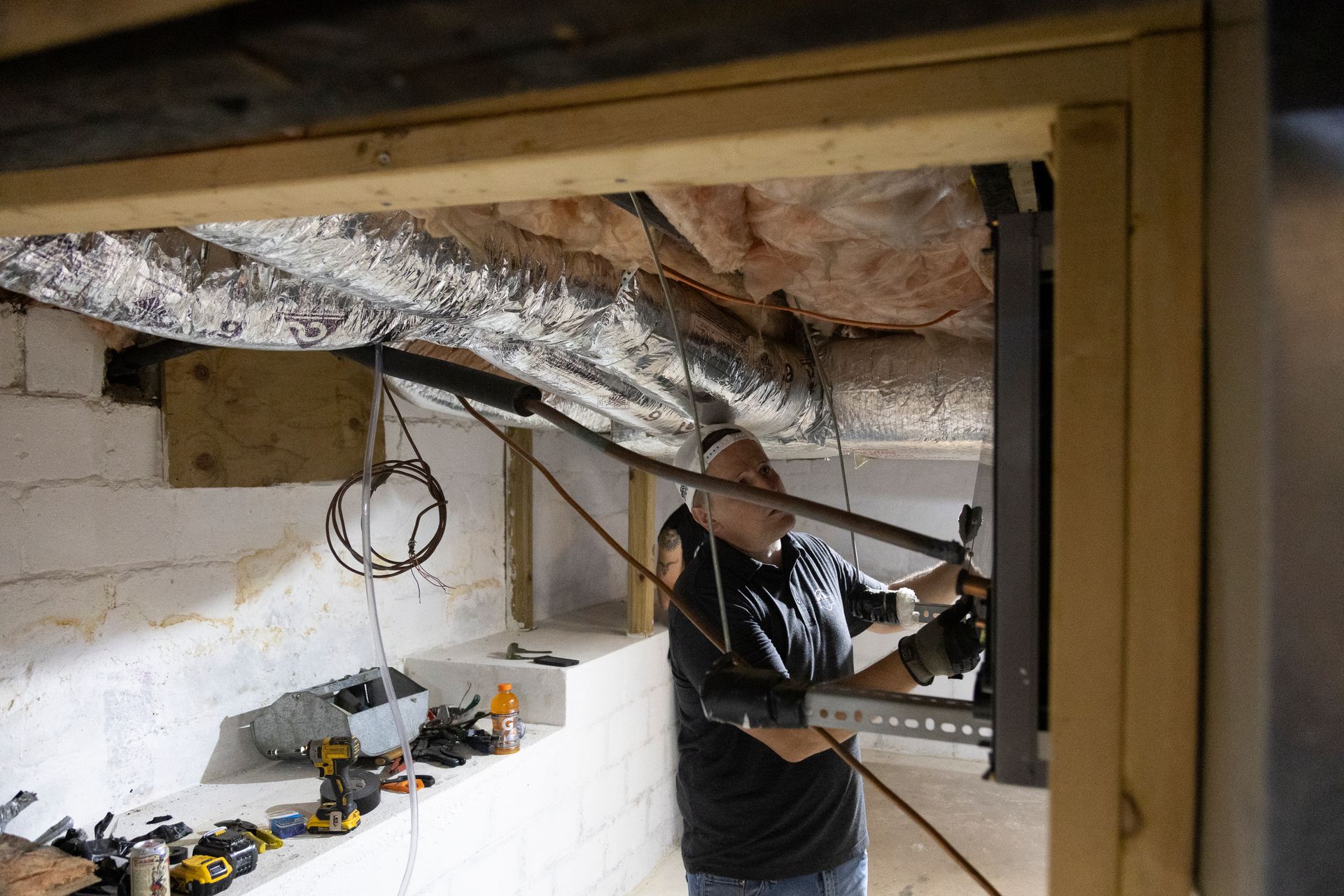 A man working on equipment in a basement. He is in the doorway with tools and wires around.