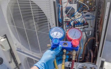 HVAC technician checking air conditioning unit with gauges; outdoors. Blue gloves, red/blue hoses.