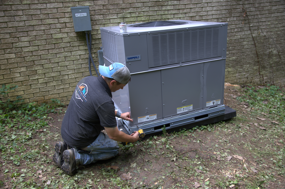 HVAC technician installing an air conditioning unit outside a brick building.