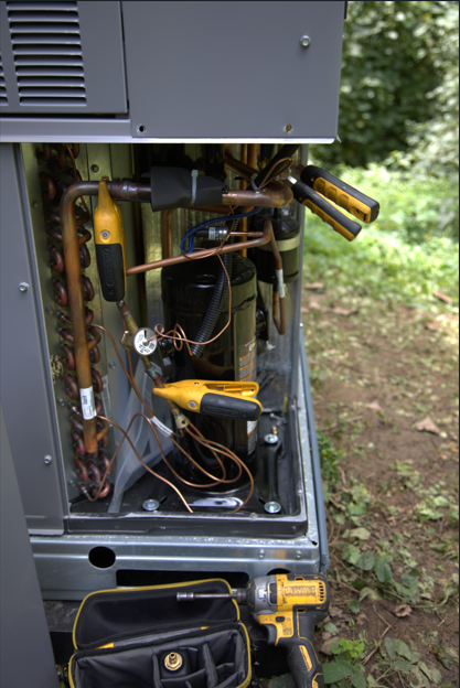 HVAC unit with exposed copper pipes and service tools outdoors.