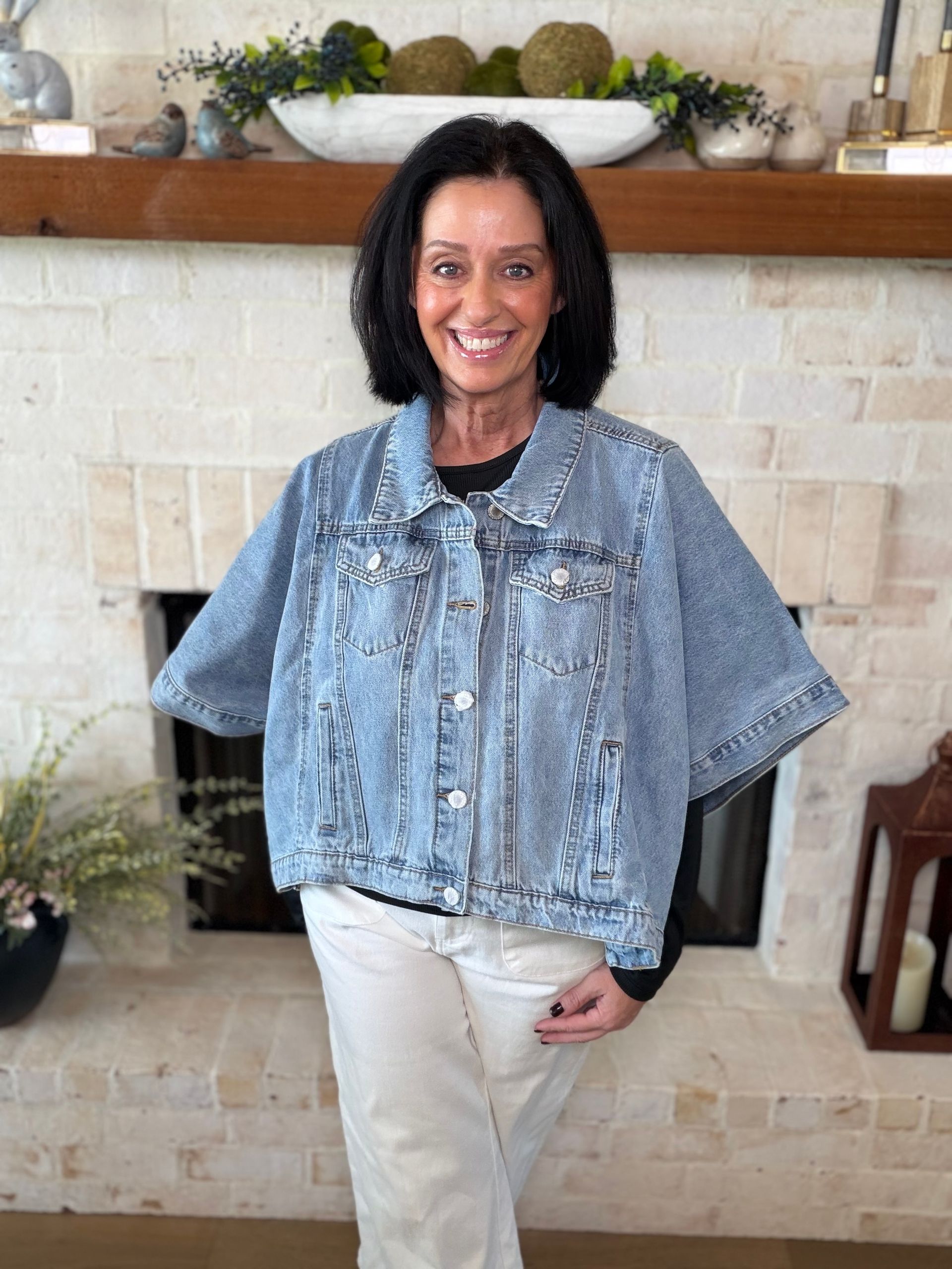Woman in denim jacket and animal print skirt smiles near brick wall.