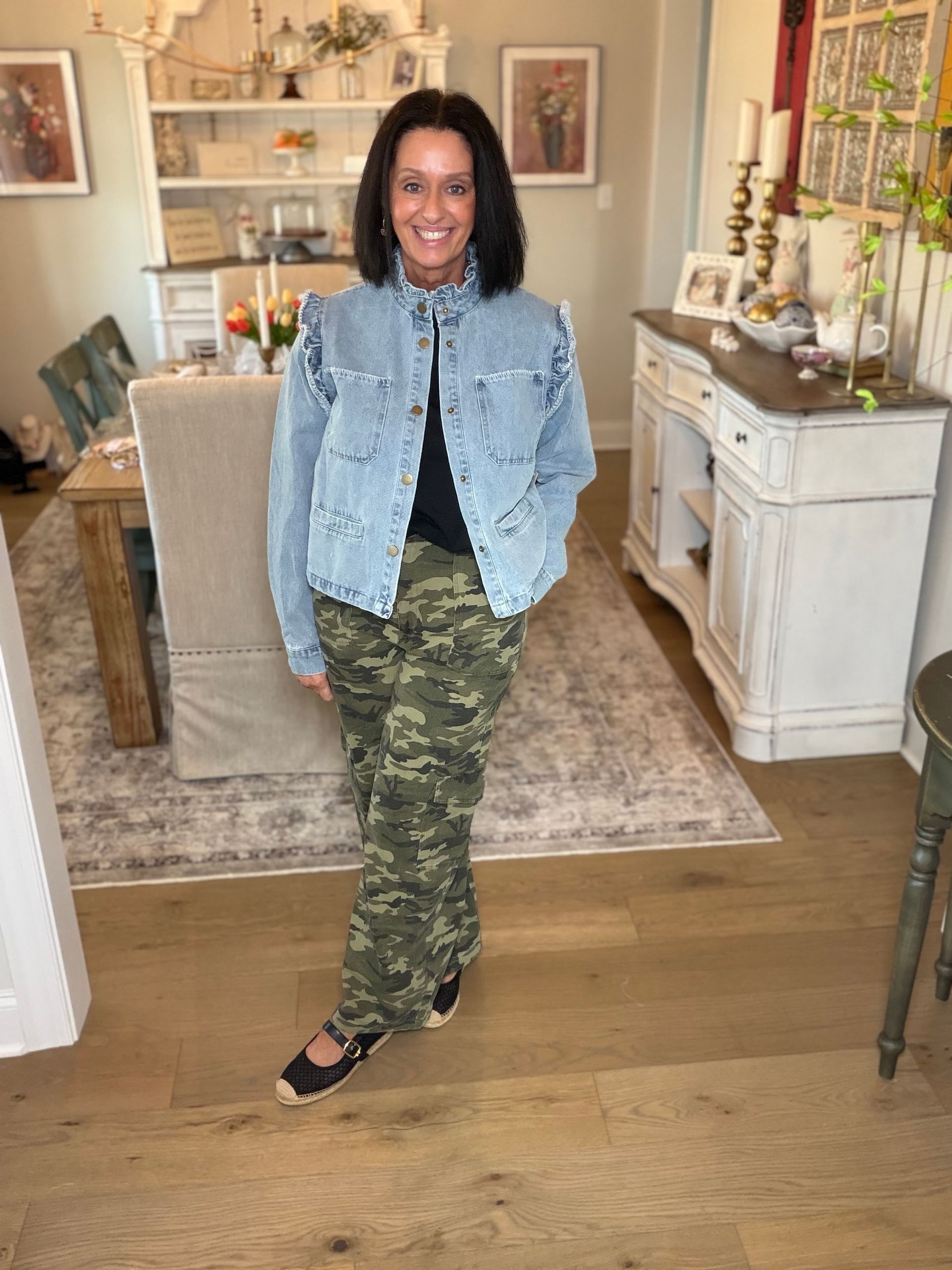 Woman in brown top and floral pants poses against a brick wall.