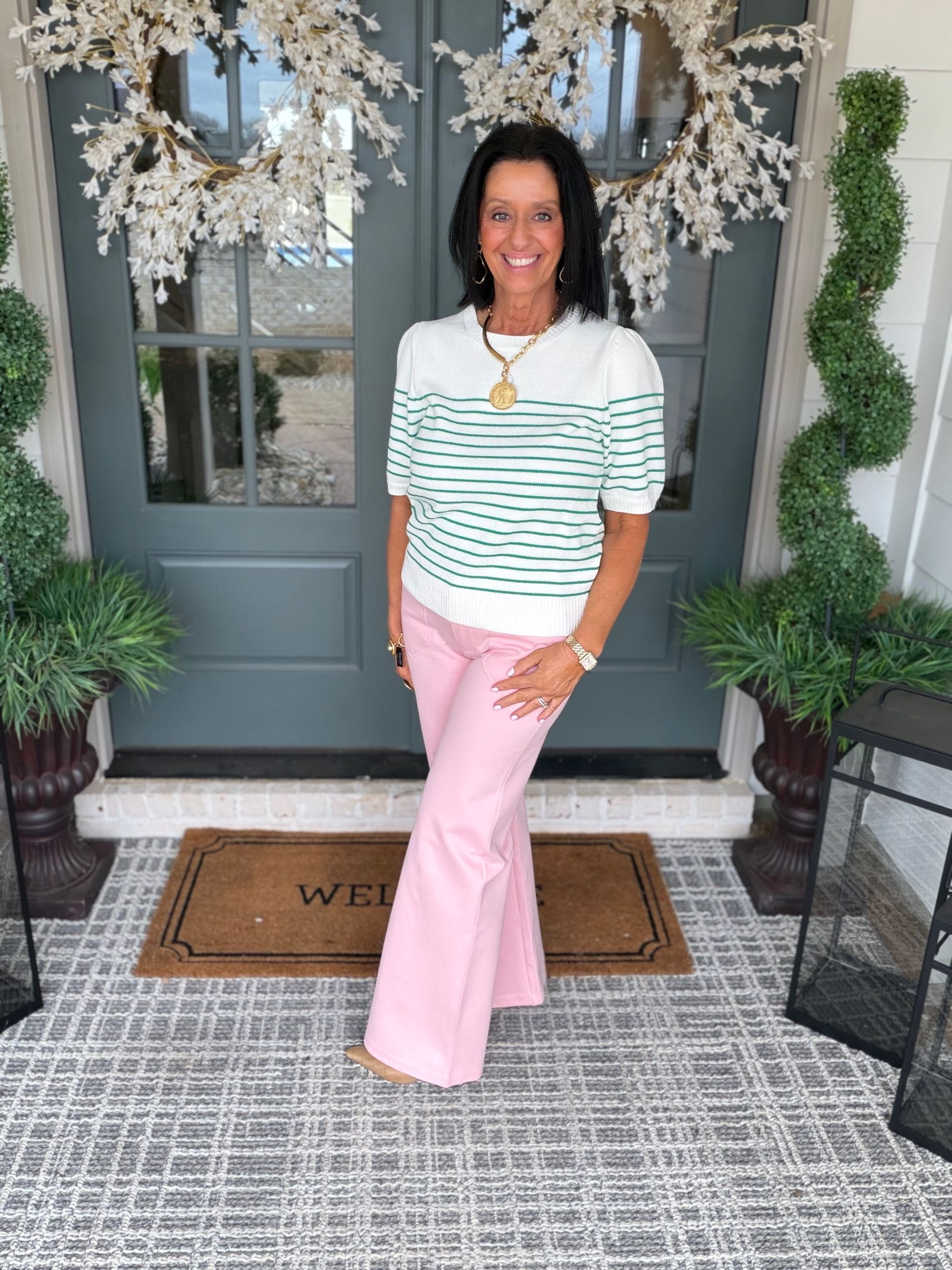 Woman in brown top and patterned pants smiles in front of a brick wall.