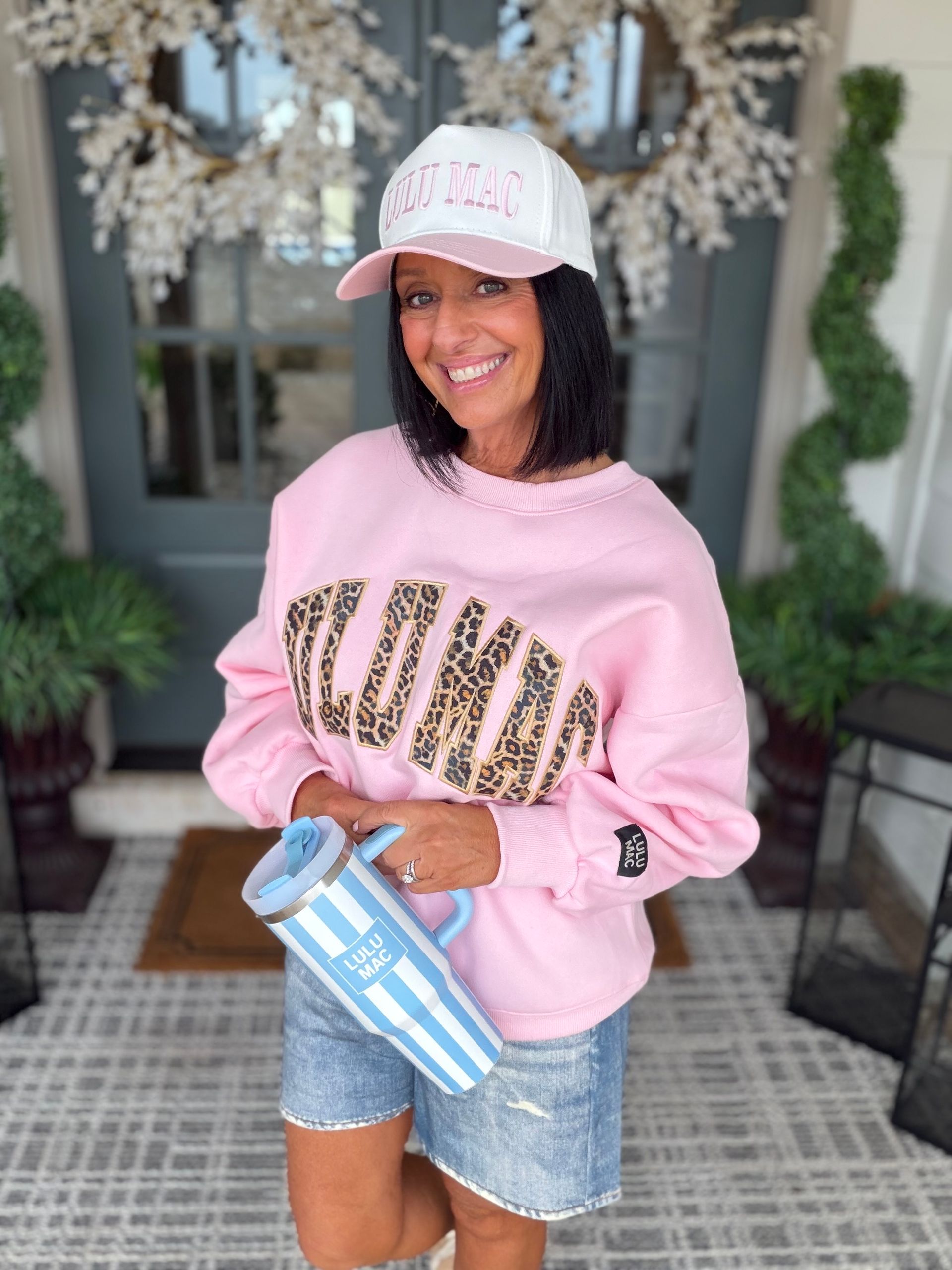 Woman in blue floral top and white pants stands in front of a brick wall.