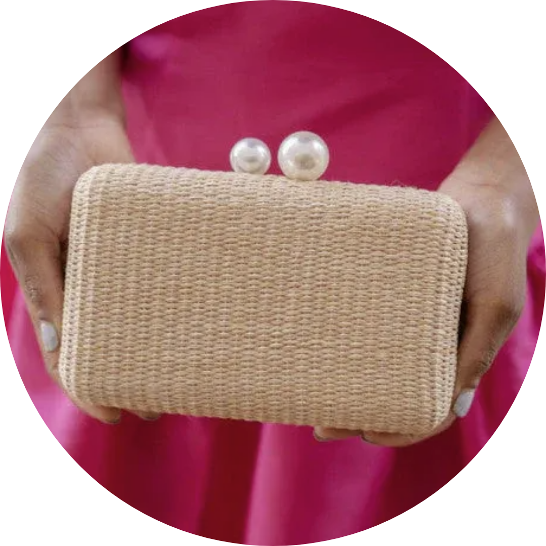 Woman in pink dress holding a beige woven clutch with pearl closure.
