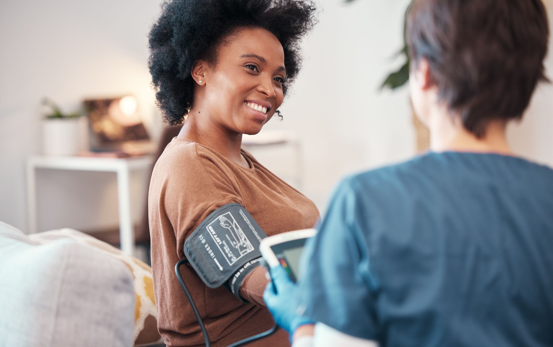 A healthcare worker takes the blood pressure of a smiling patient during a home visit.