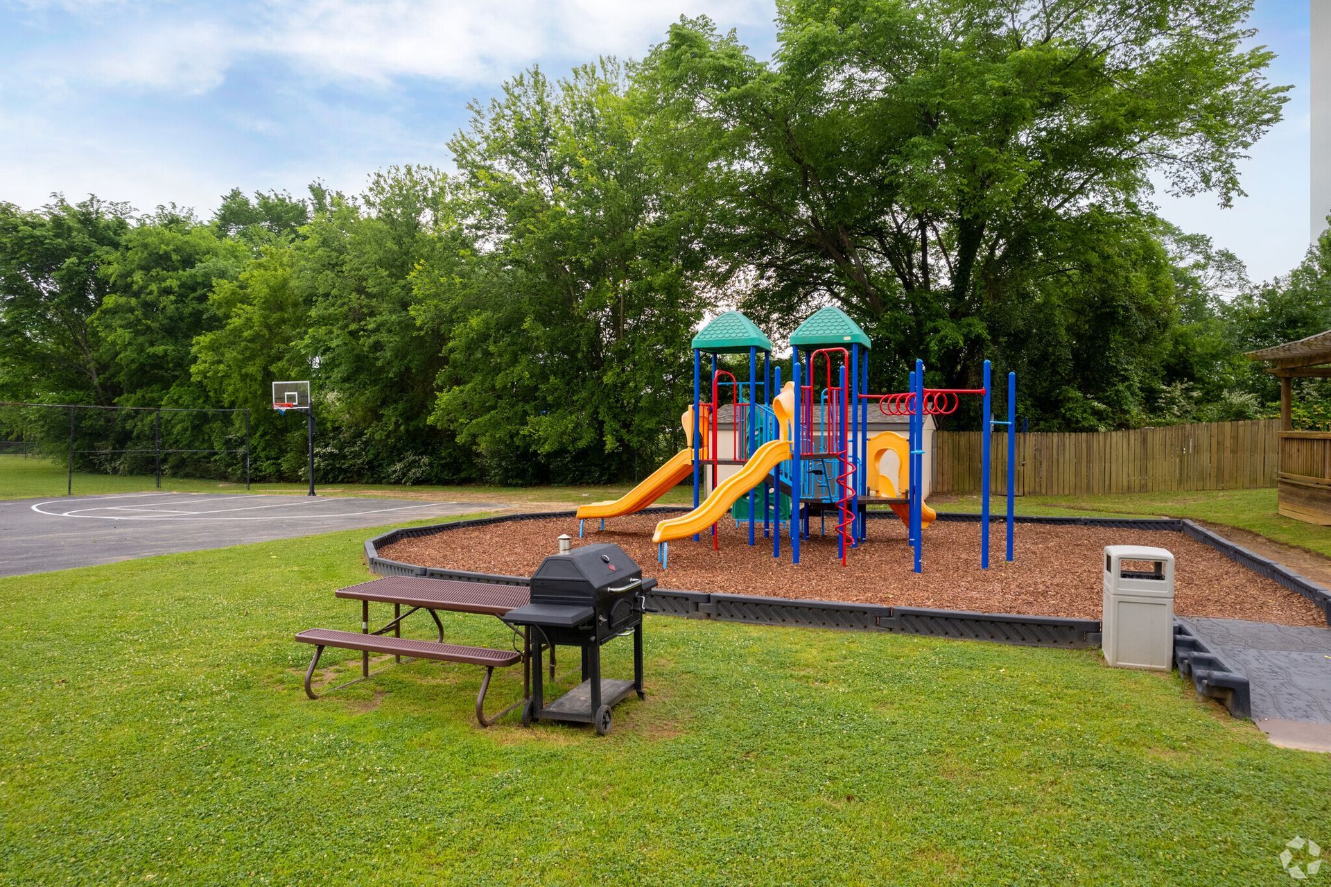 A playground with a grill and a picnic table in the grass.