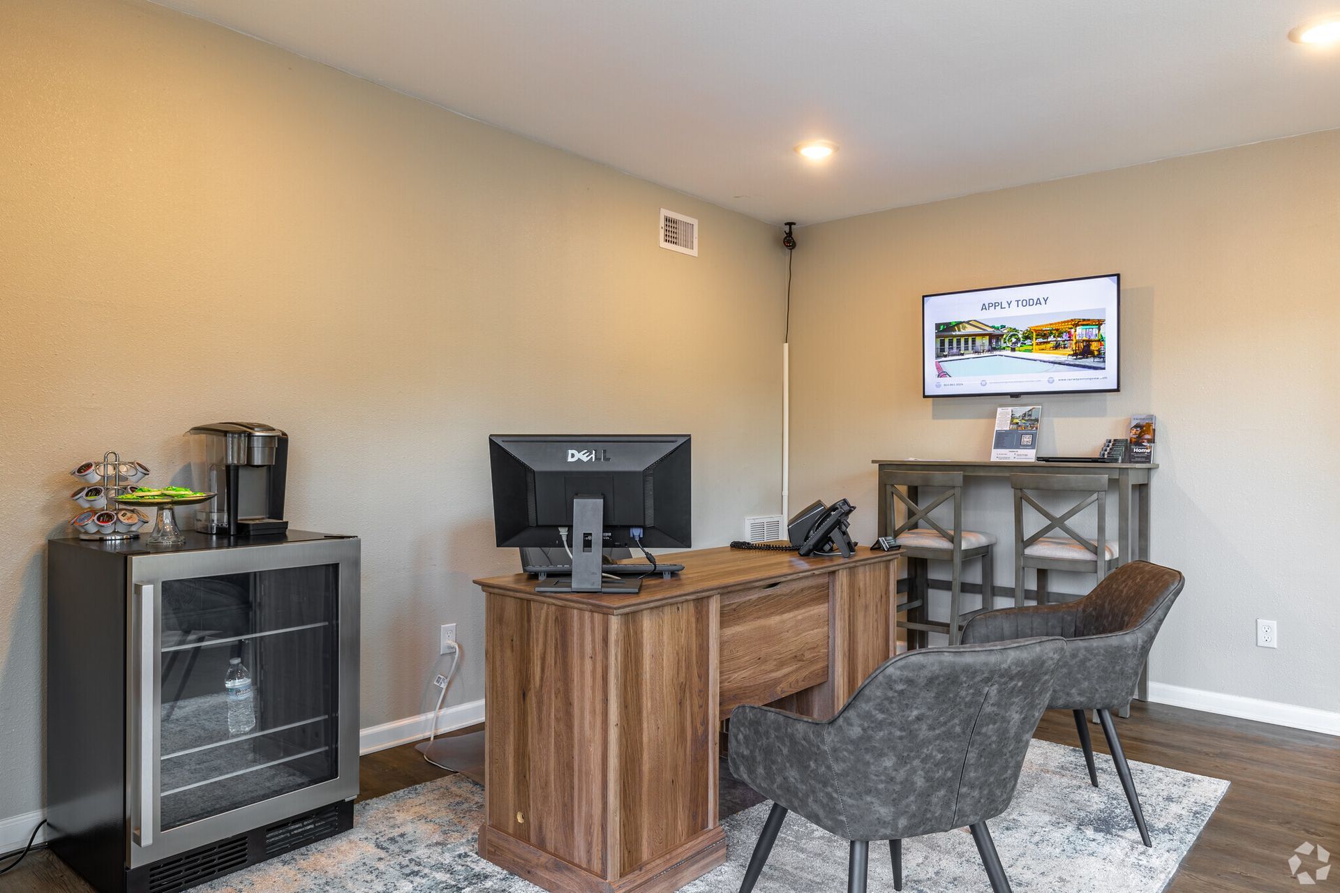 A room with a desk , chairs , a television and a refrigerator.