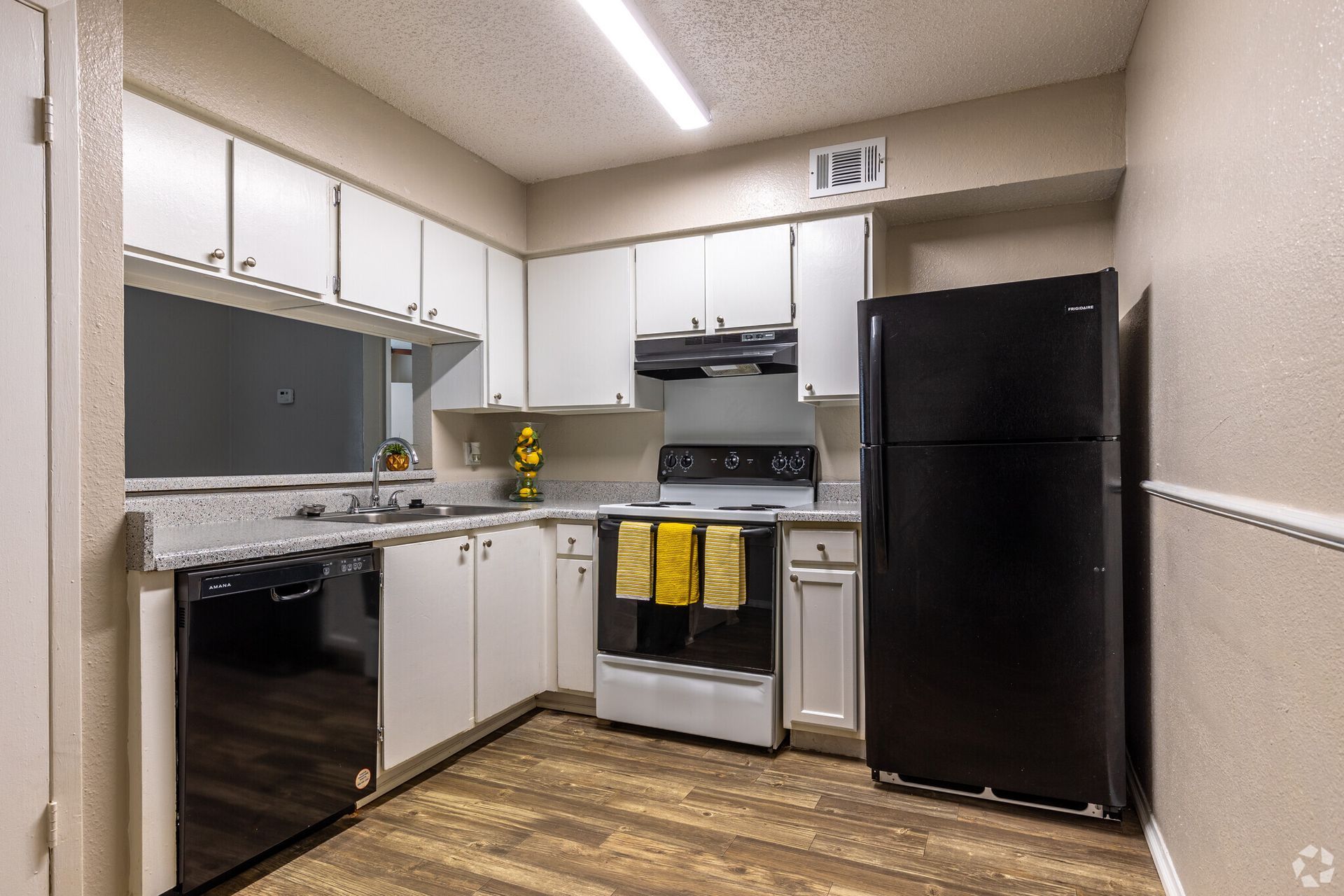 A kitchen with white cabinets , a black refrigerator , a stove , and a dishwasher.