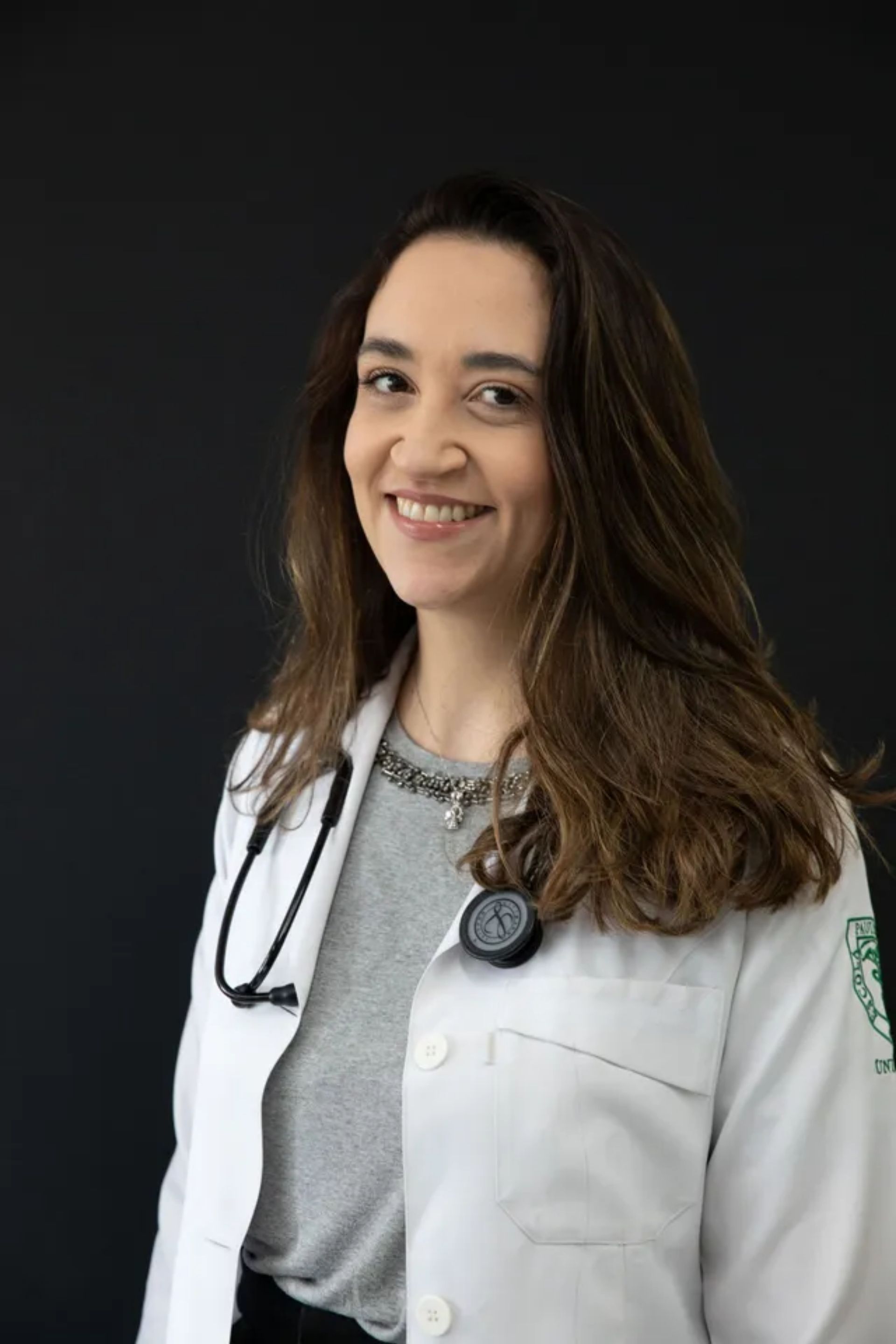 Uma mulher de jaleco com um estetoscópio no pescoço está sorrindo.