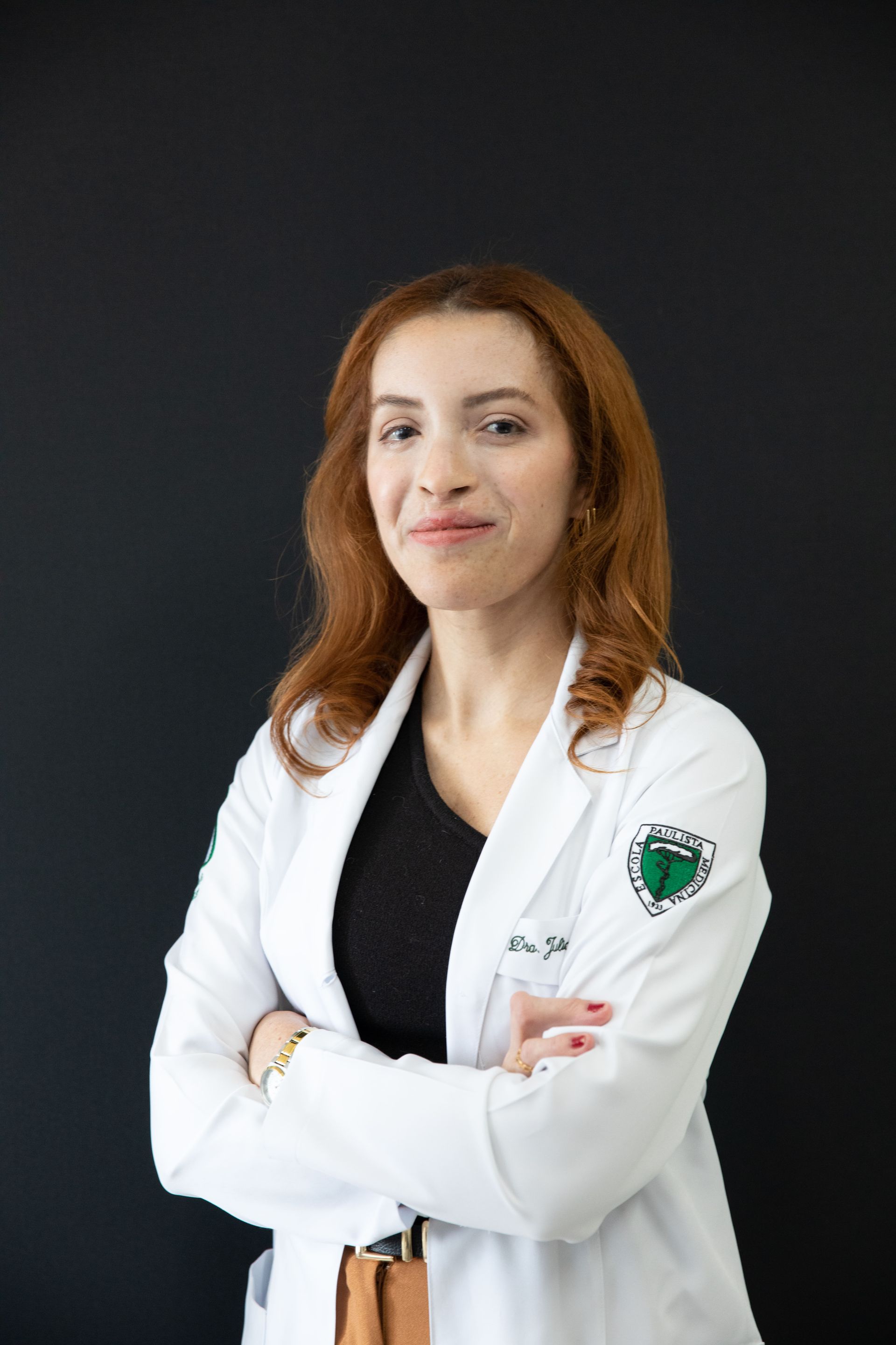 Uma mulher de jaleco branco está de pé com os braços cruzados.