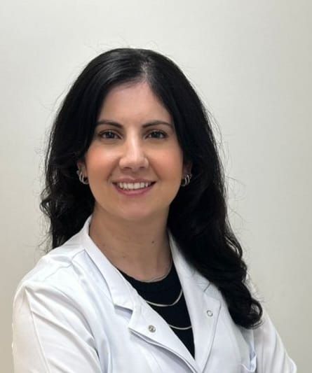 Uma mulher de jaleco branco sorri para a câmera