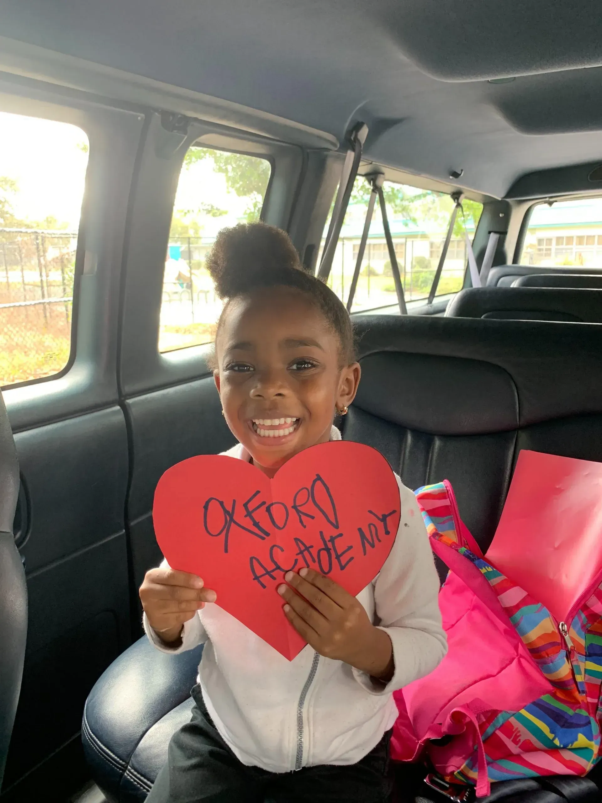 Young girl in vehicle holding a red heart with text 
