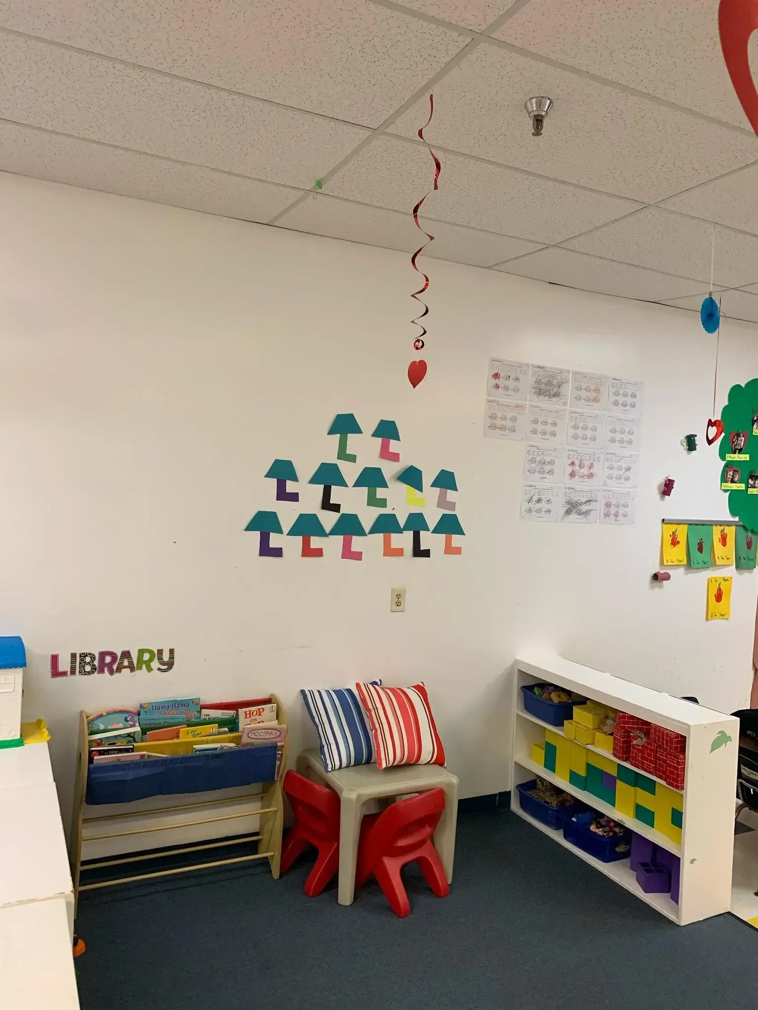 Child's library area with books, chairs, decorations, and storage shelves in a classroom setting.