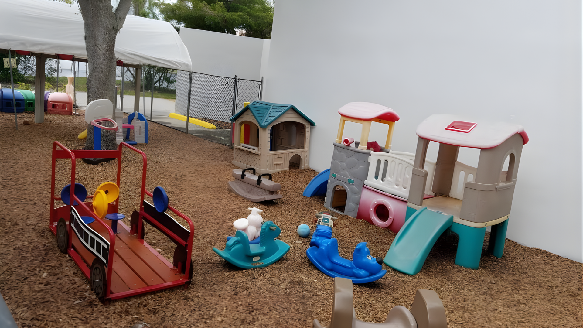 Playground with brown pebbles, toy houses, fire truck, and rocking toys.