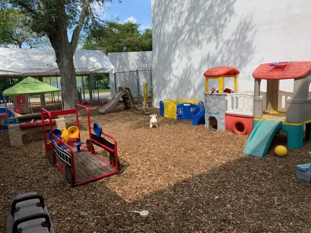 Playground with wood chips, slides, and toy structures. A small animal is in the center.
