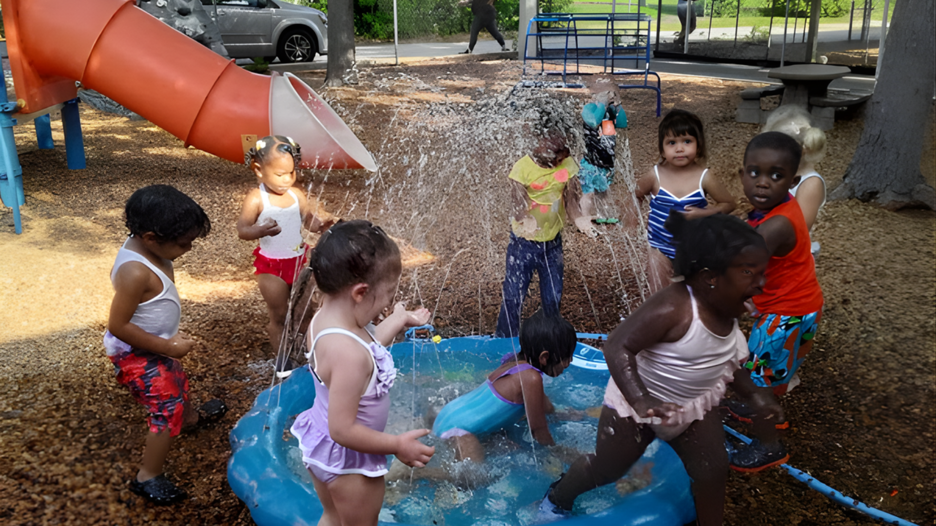 Children playing in a splash pad at a park, near a slide, water splashing.