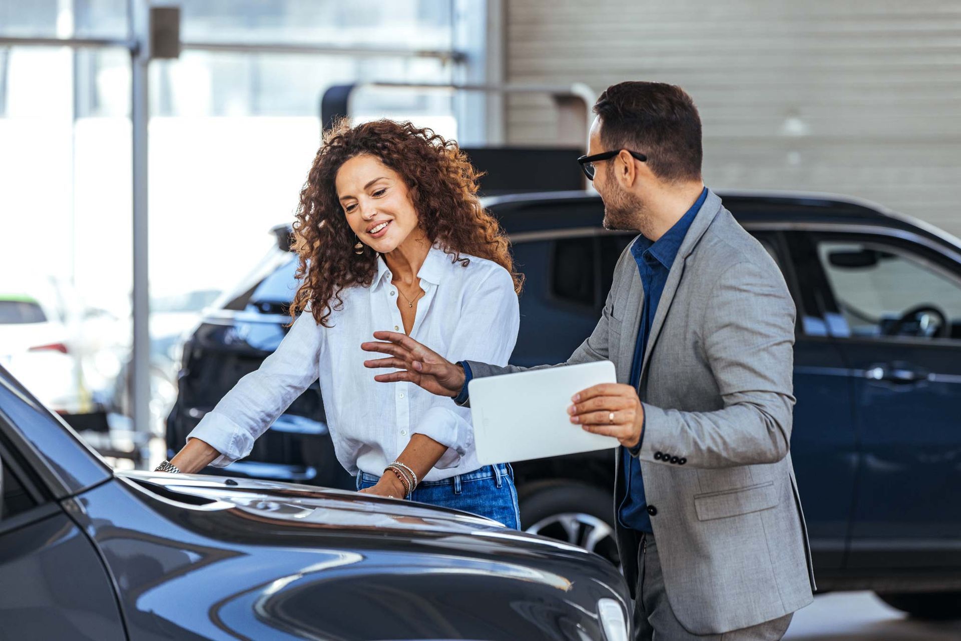 A man and a woman are looking at a car in a showroom.