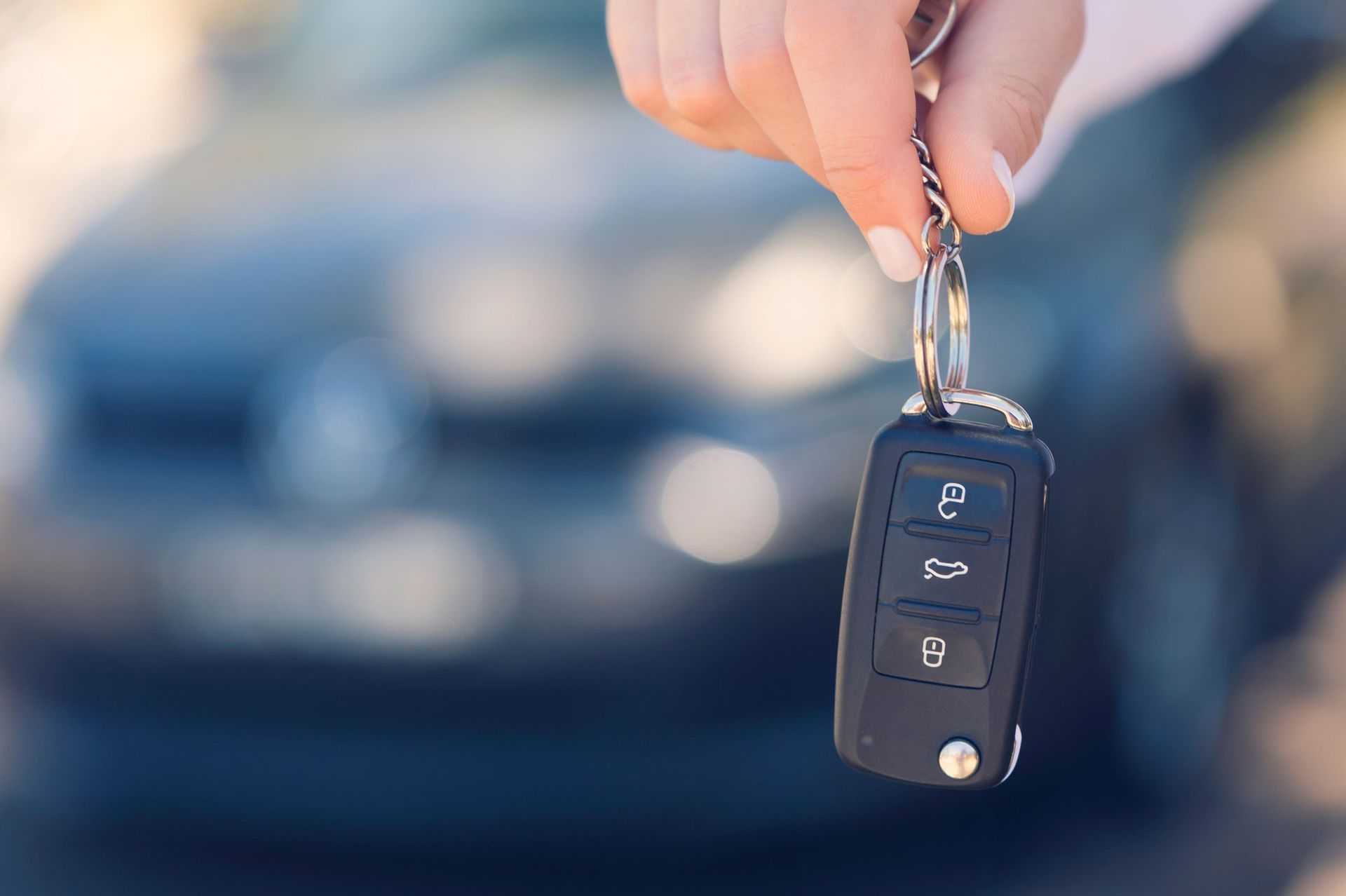 A person is holding a car key in front of a car.