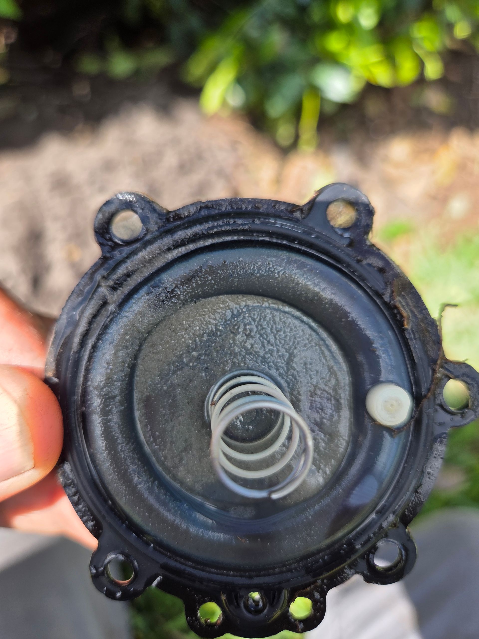 Black circular part with a spring and small white disc. Held in a person's fingers.