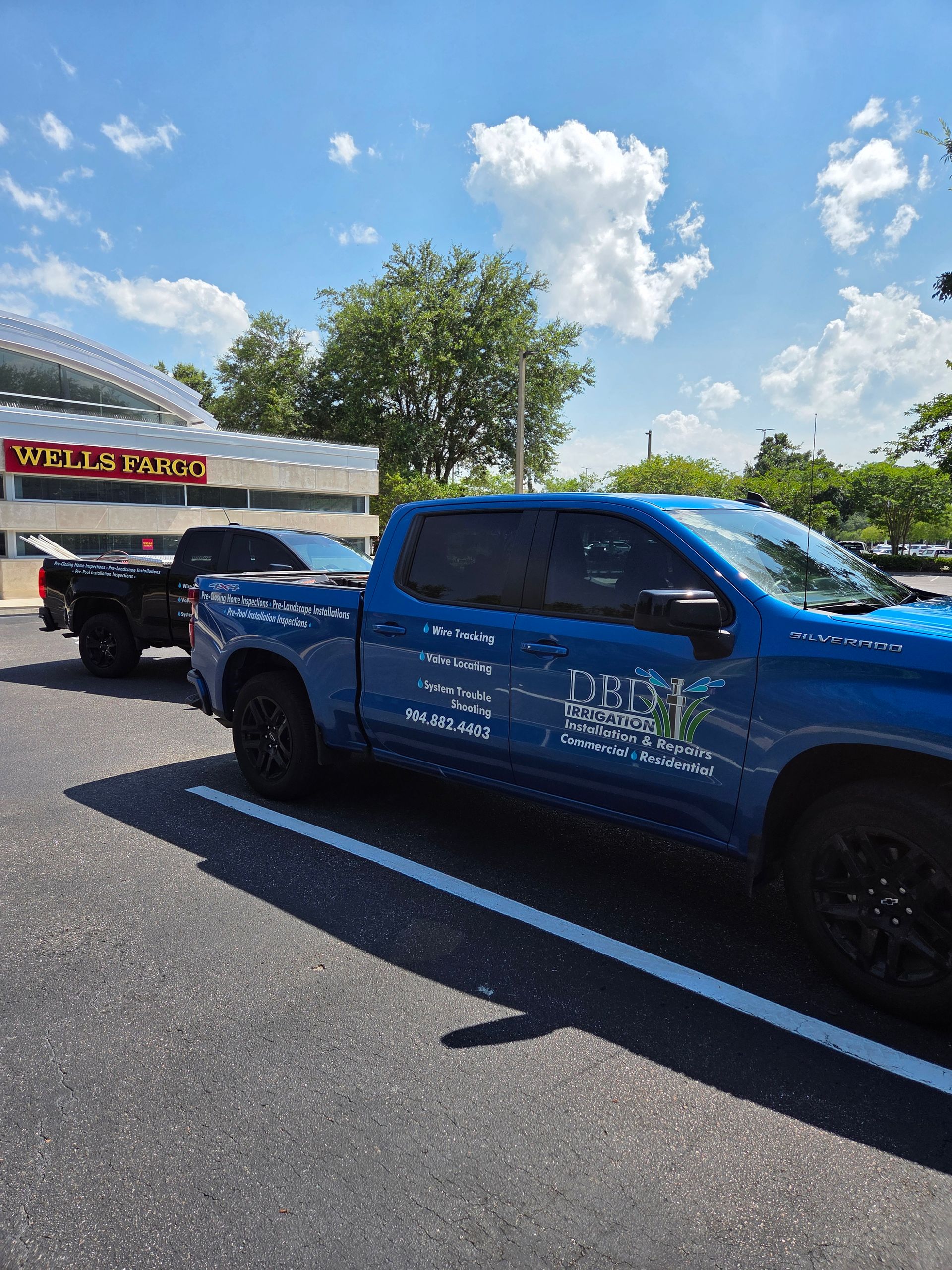 Blue pickup truck with logo parked next to a black truck in a parking lot. Wells Fargo sign in the background.