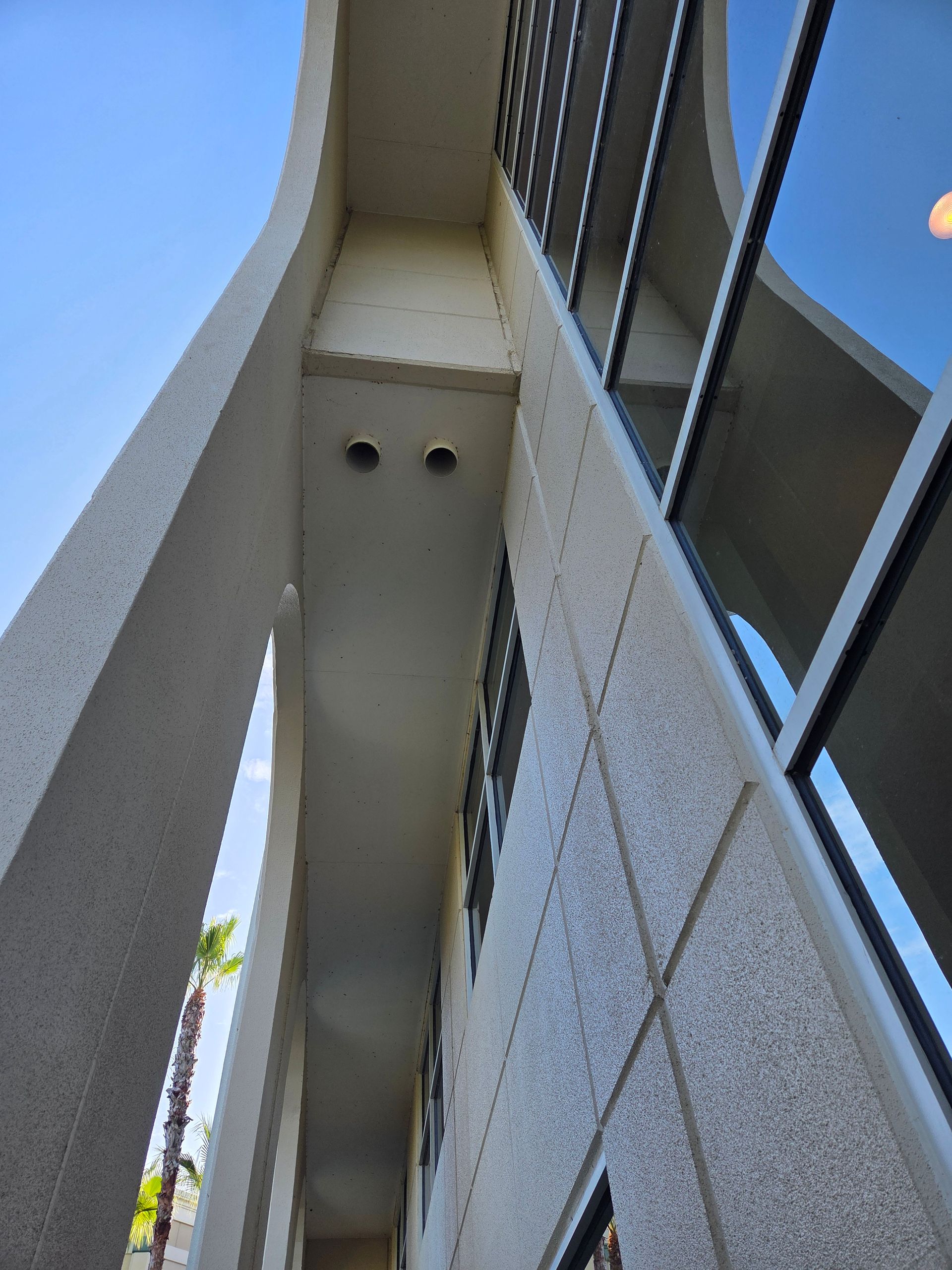 Low-angle view of a building's exterior with textured walls, windows, and an arched walkway. Sky visible.