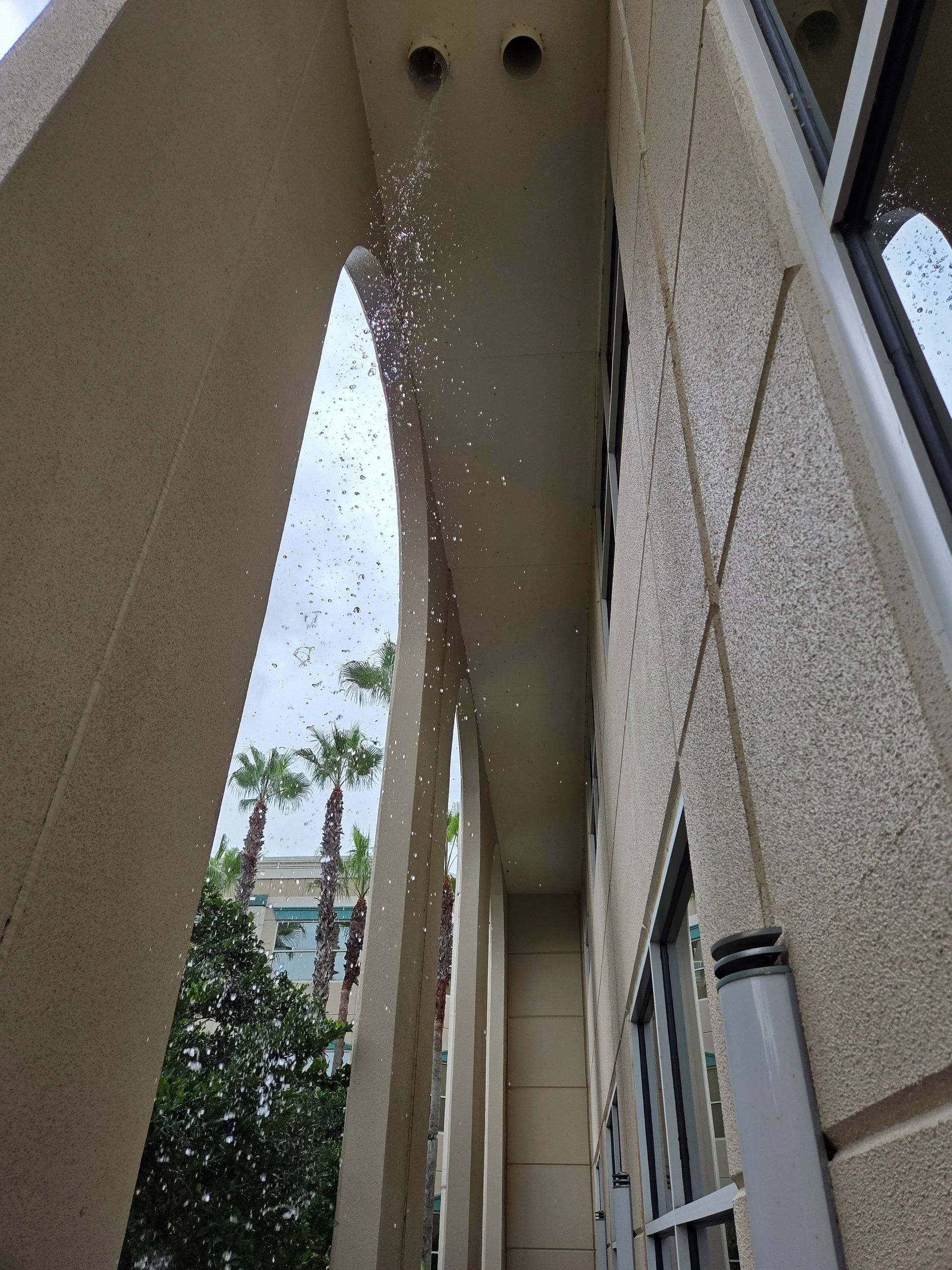 View up an archway, possibly a building entrance, with water droplets suspended mid-air. Palm trees visible.