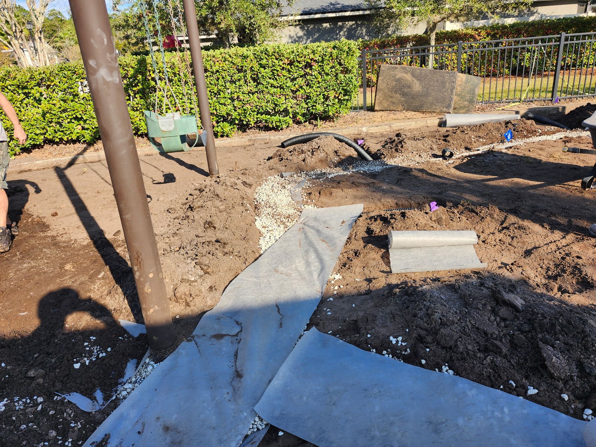 Construction site: dirt, pipes, pavers, and a brown pole. A person's shadow is visible.