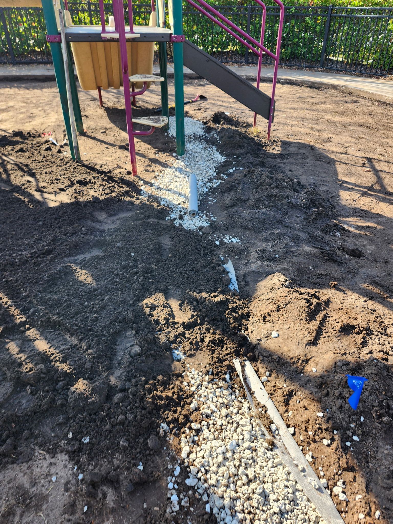 Trench filled with gravel runs along the side of a playground slide. Construction site.