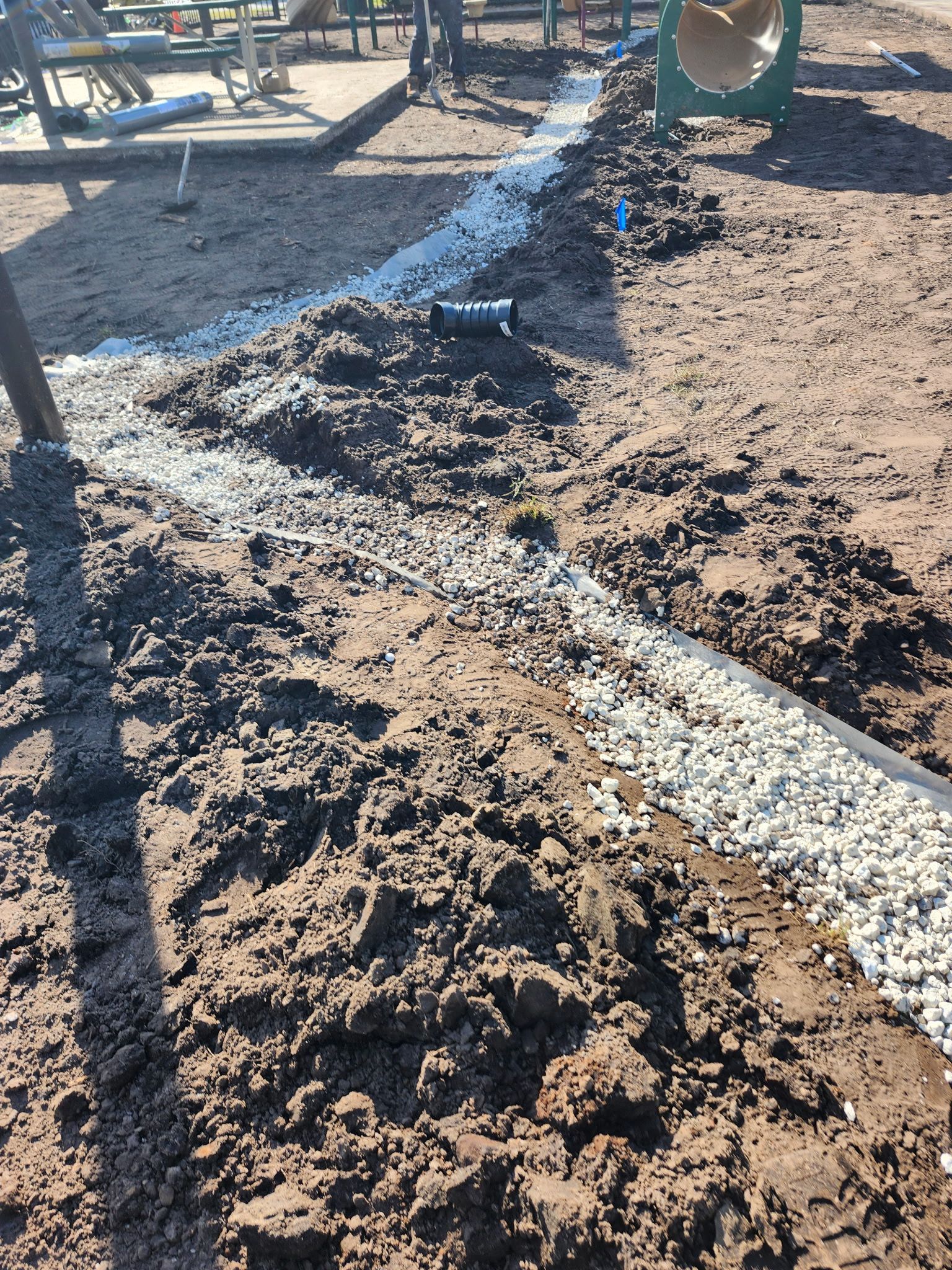 A trench filled with gravel and a pipe, likely for drainage, in a playground.