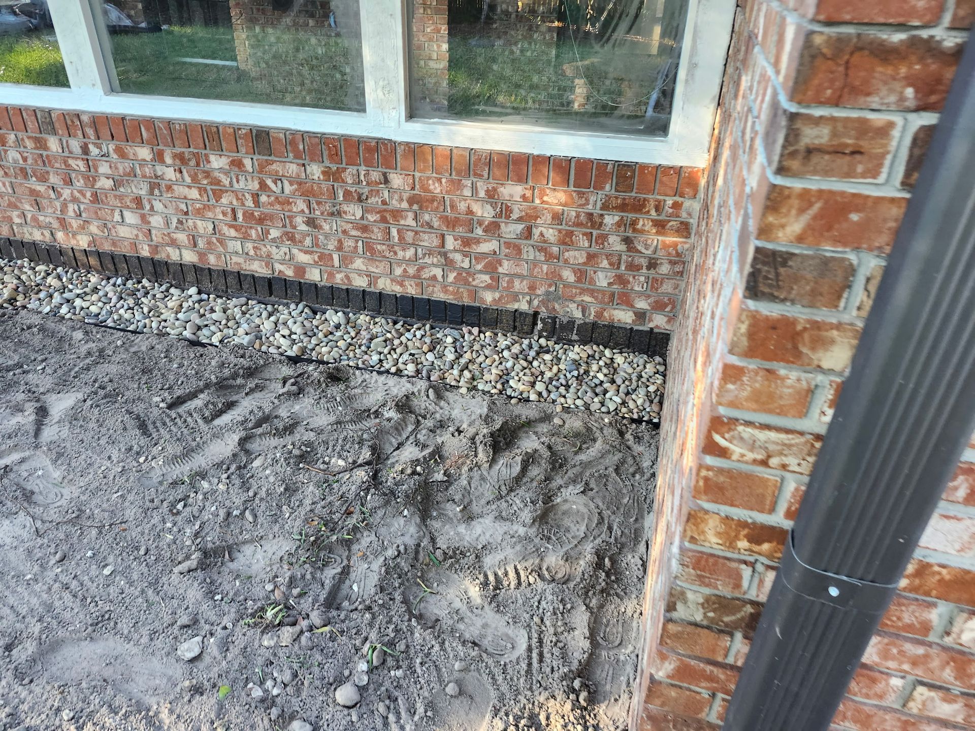 Brick building with gravel border and gutter. Sandy ground in the foreground.