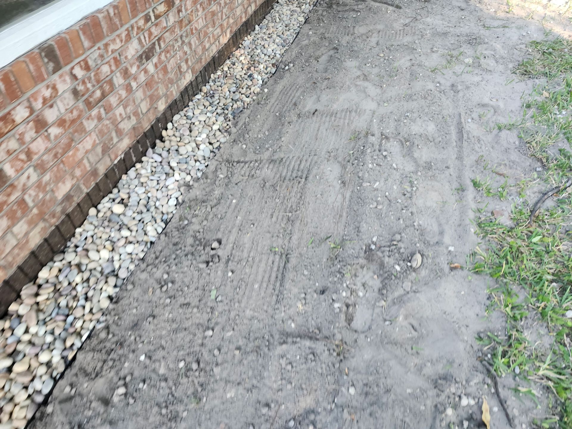 Gravel border along brick wall and dirt ground, next to grassy area.