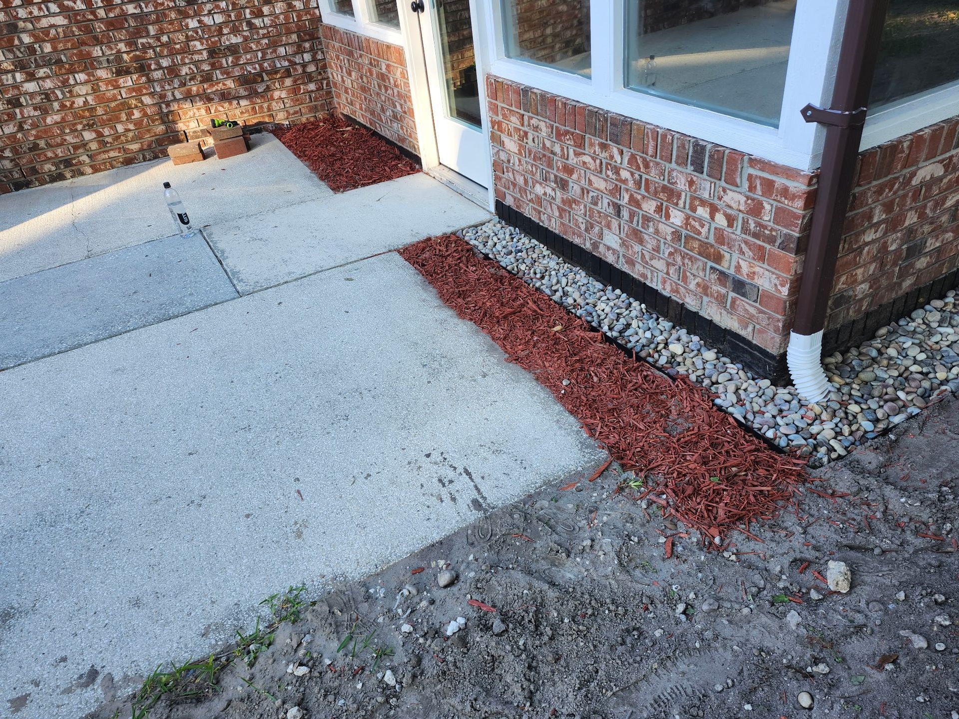 Exterior view of a building with brick walls, concrete path, and red mulch borders.