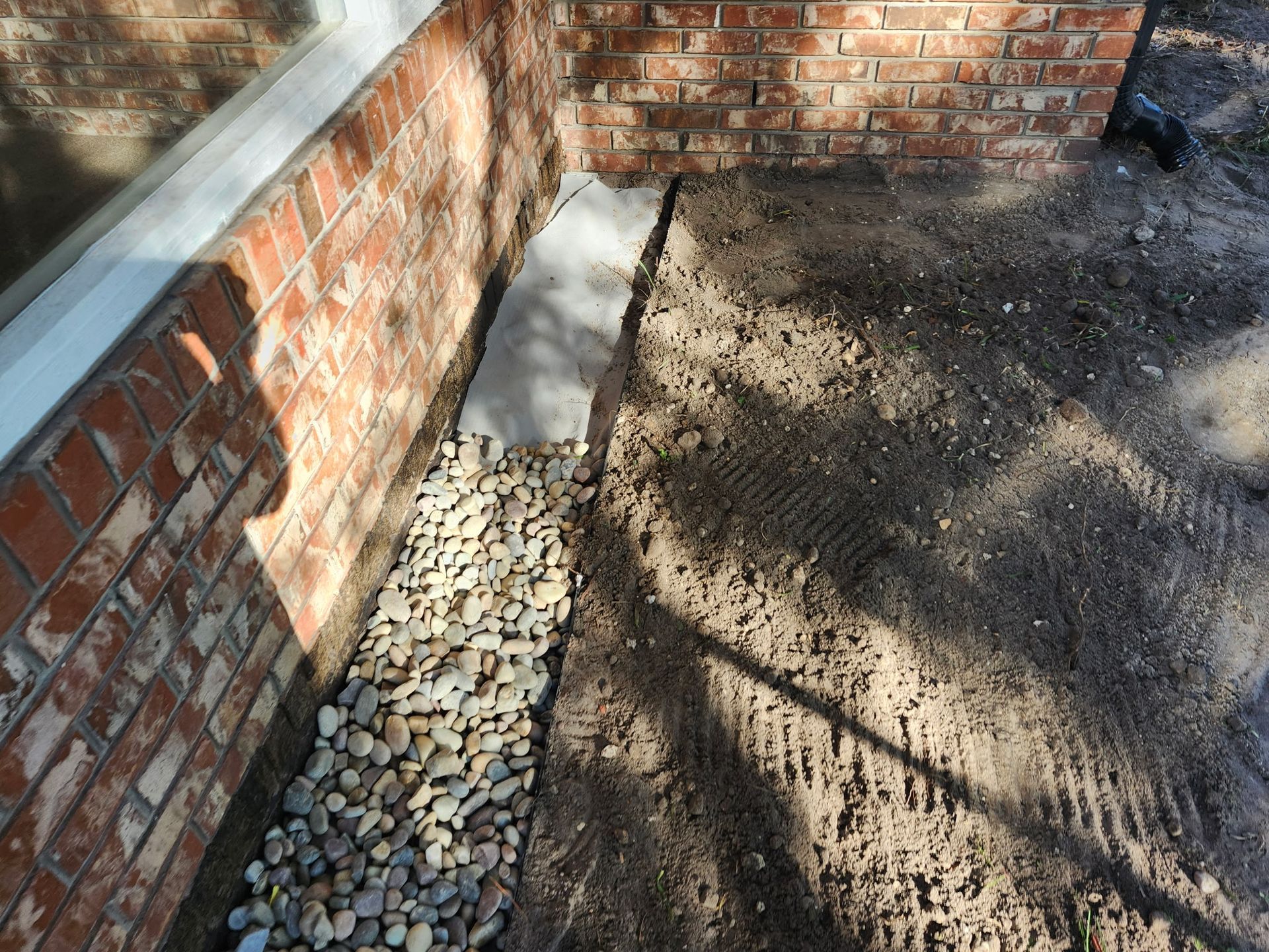 Brick wall with gravel drainage alongside a window and dirt.