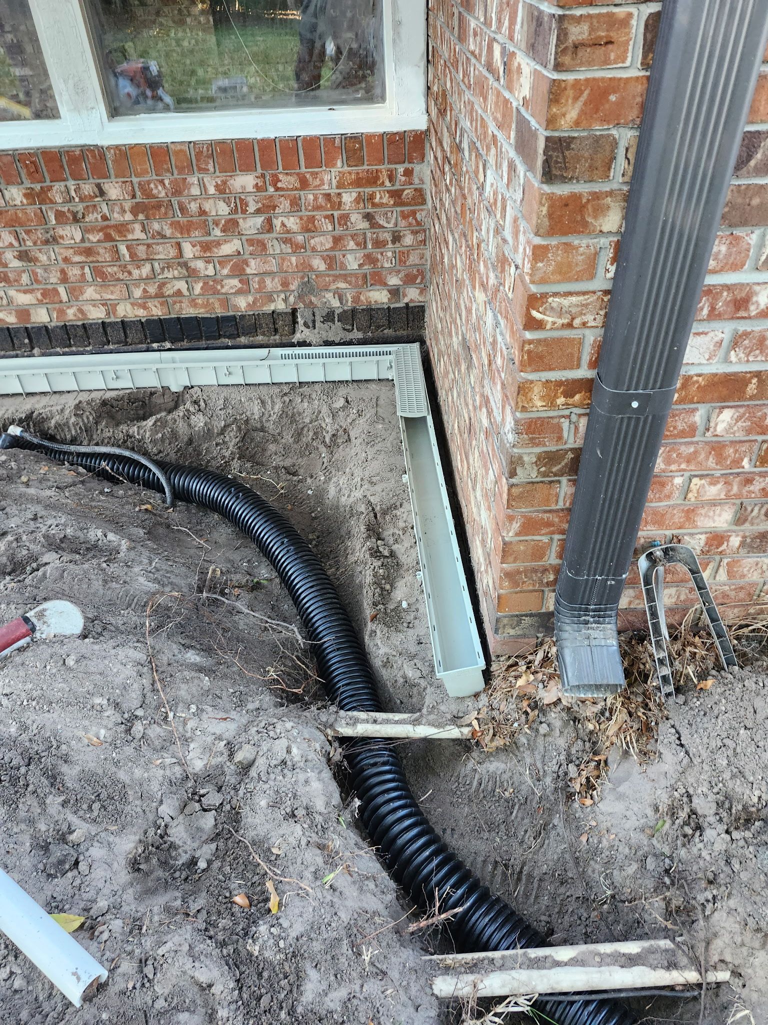 Black corrugated drainage pipe extending from gutter next to brick house.