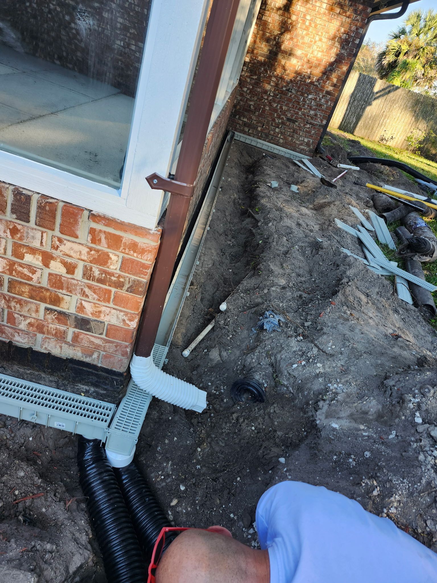 Gutters and a drain are installed along a building's brick exterior; a person looks down.
